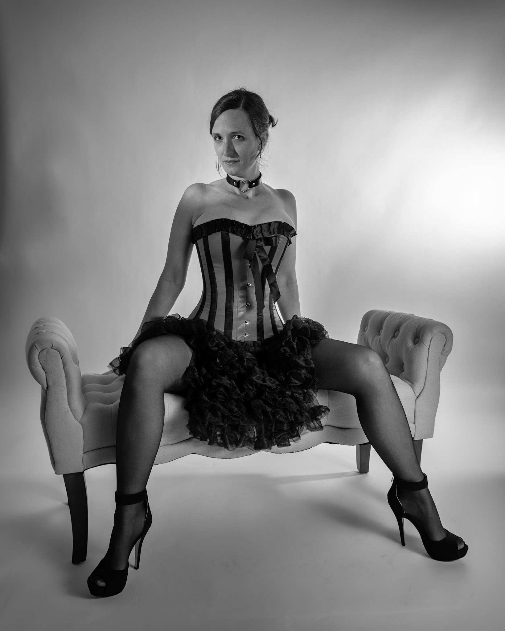 Western Corsetry - Posing on the Fainting Couch (B&amp;W): Bringing back out the western themed corset outfit for a final run at studio shots with the seamless backdrop. Godox v1 with 7" reflector front left, 30x120 softbox with another Godox V1 right side, and Godox AD200 w/ Yellow gel lighting the backdrop.