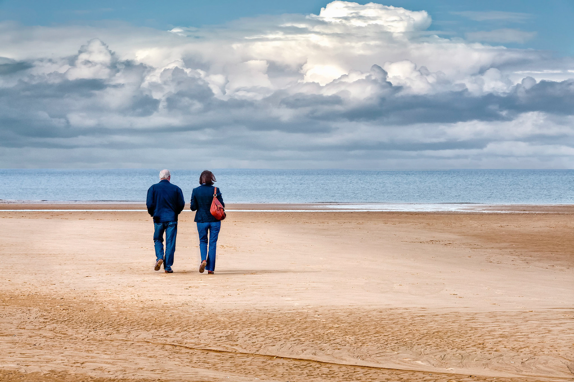 Rugged up against a cool sea breeze and seeking some alone time, a couple walks in solitude along the deserted Holkham Beach in Norfolk, UK.