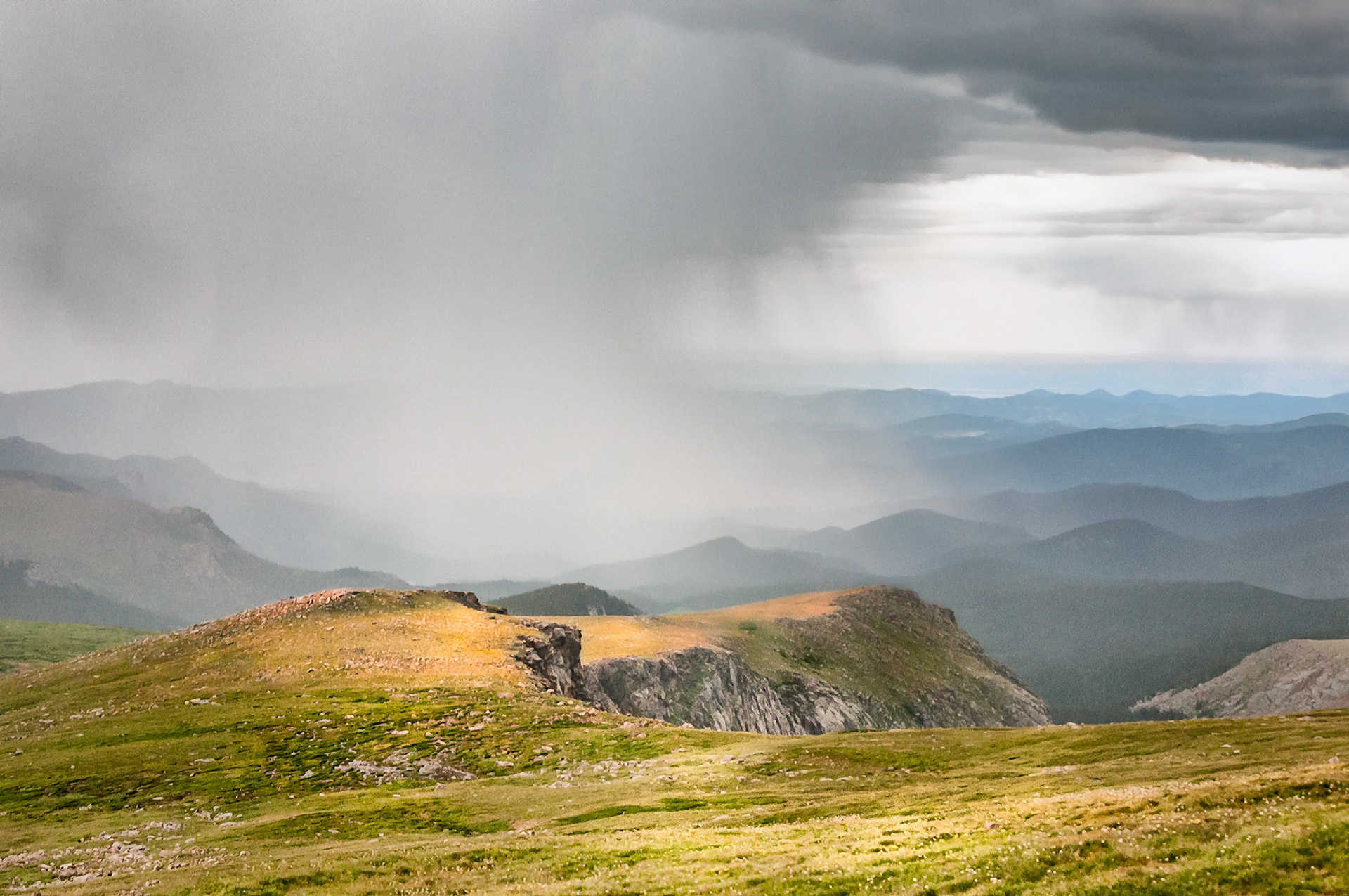 Sunlight filters through breaks in the clouds as an intense rain shower buckets down into the headwaters of Bear Creek in the Mount Evans Wilderness area near Denver, Colorado.