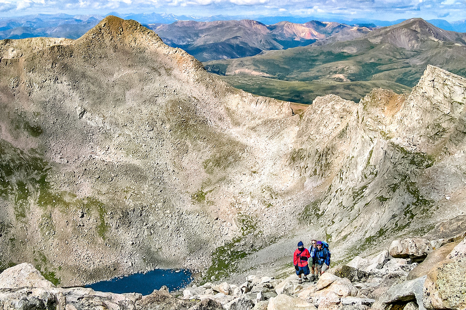 A group of hikers work their way up Mount Evans, (14,265 feet = 4,348m), as they enjoy splendid views of Abyss Lake, (12,650 feet = 3,856 meters), Mount Bierstadt, (14,060 feet = 4,285m), and The Sawtooth skyline. Beyond lies Guanella Pass and mountains of the USA Continental Divide.