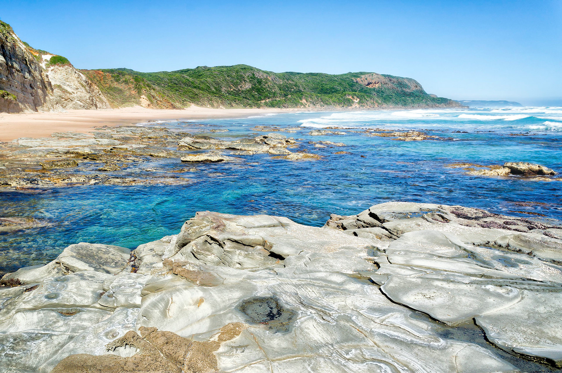 A clear blue sky reflects in rock pools along the shoreline of the Great Otway National Park, near Apollo Bay, Victoria, Australia. The vast beaches, devoid of tourist crowds, stretch between rocky headlands and inlets along the coastline. Protected from the pounding surf by rocky reefs, these pools are a snorkeler's delight.