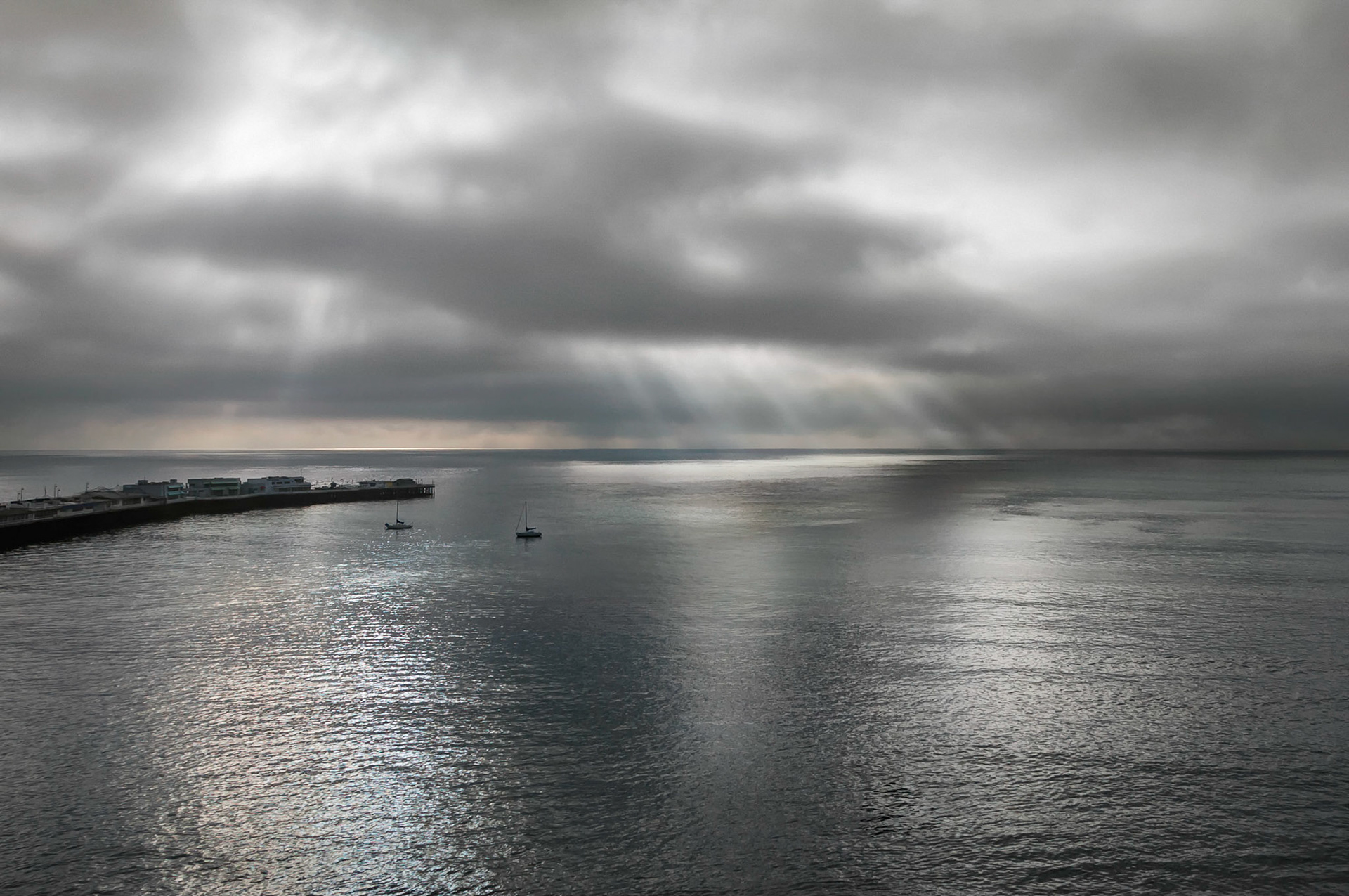 Sun rays begin to peek through to illuminate the sea as a morning fog lifts away from Monterey Bay, California. A gloomy start soon dissipates, giving way to a bright, sunny and cheerful blue sky day.
