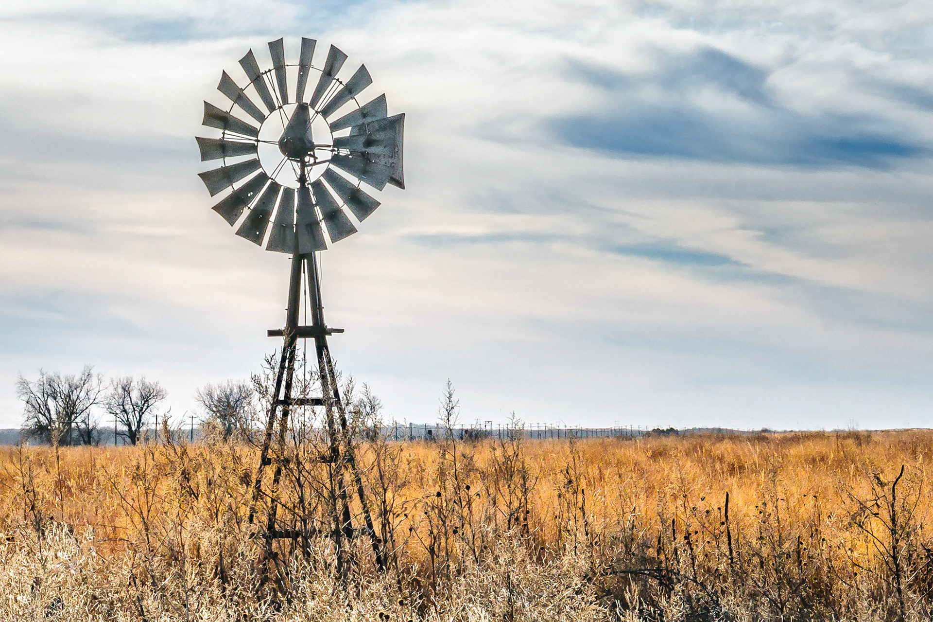 An idle old windmill turns in the breeze on a Nebraska ranch in a field of native pasture grasses. No longer needed to provide water, it has become a relic of a bygone age.