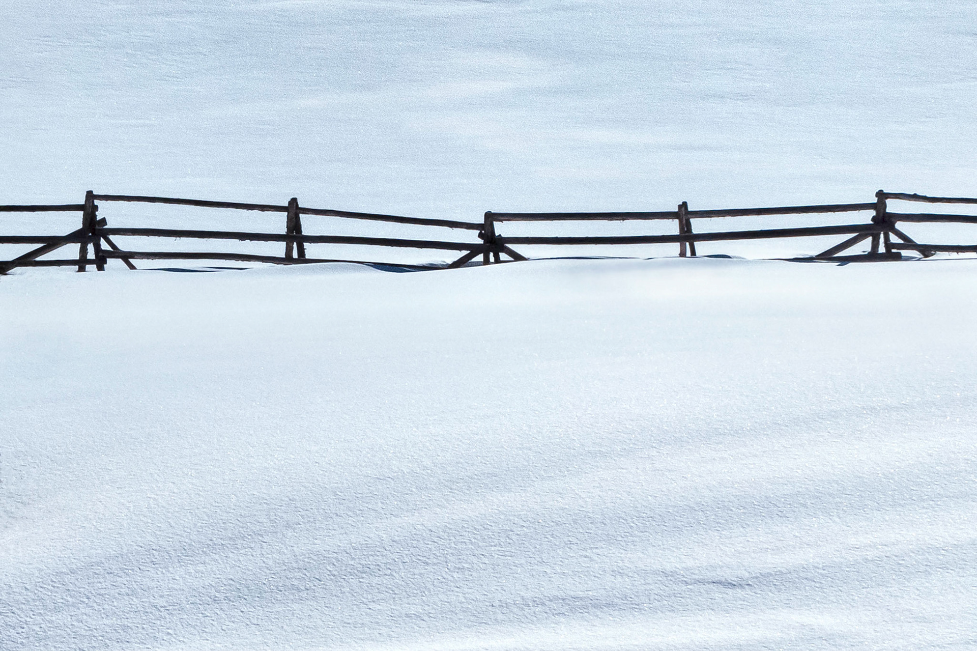 An old and weathered log fence marks property boundaries and divides pasture lands in the high country of Colorado, USA. Drifting snow covers the pastures and the afternoon shadows create interesting textures on the landscape.