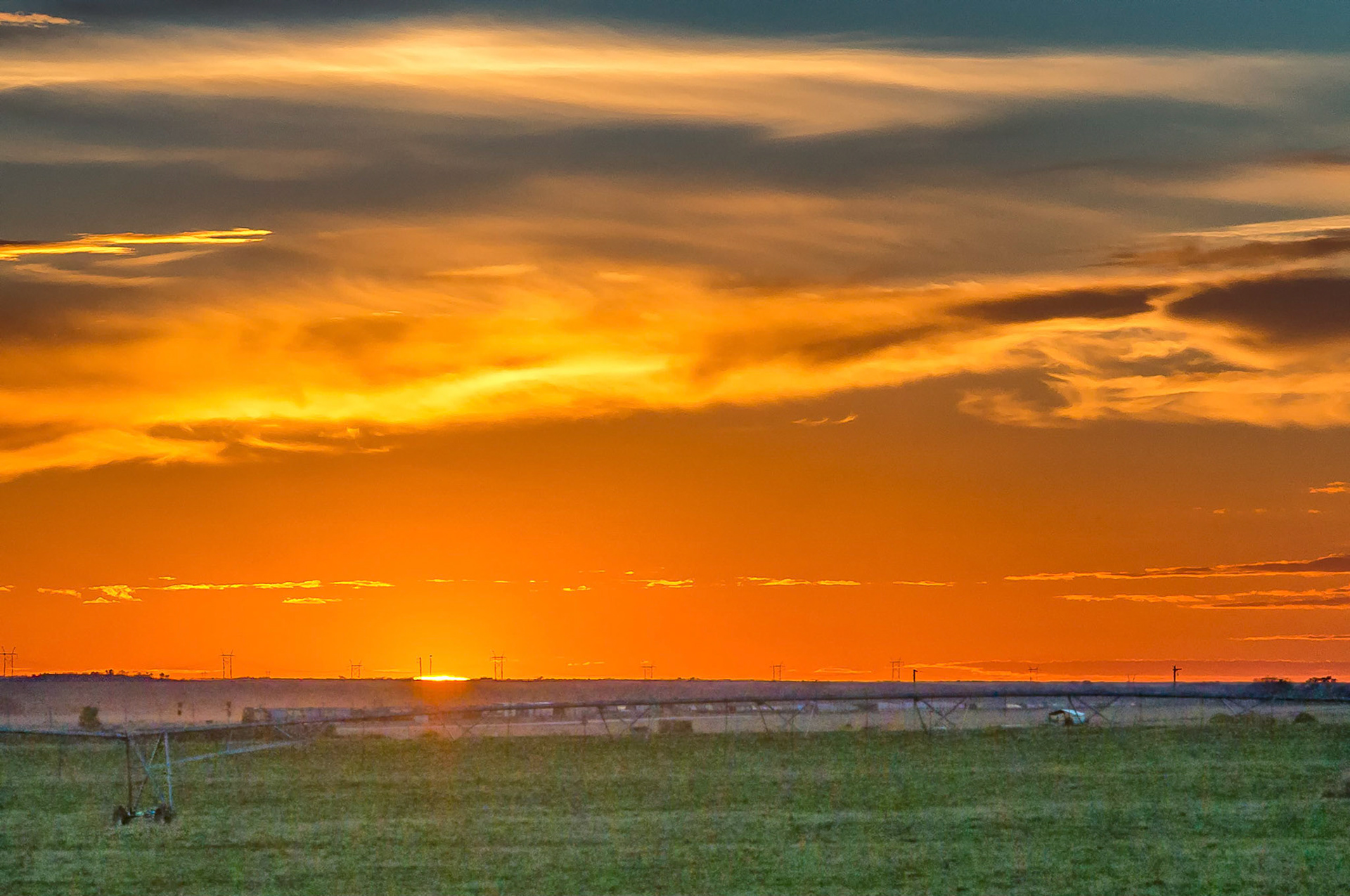A vivid orange sky intensifies as the setting sun catches the clouds over ranch lands near Paxton, Nebraska, USA.