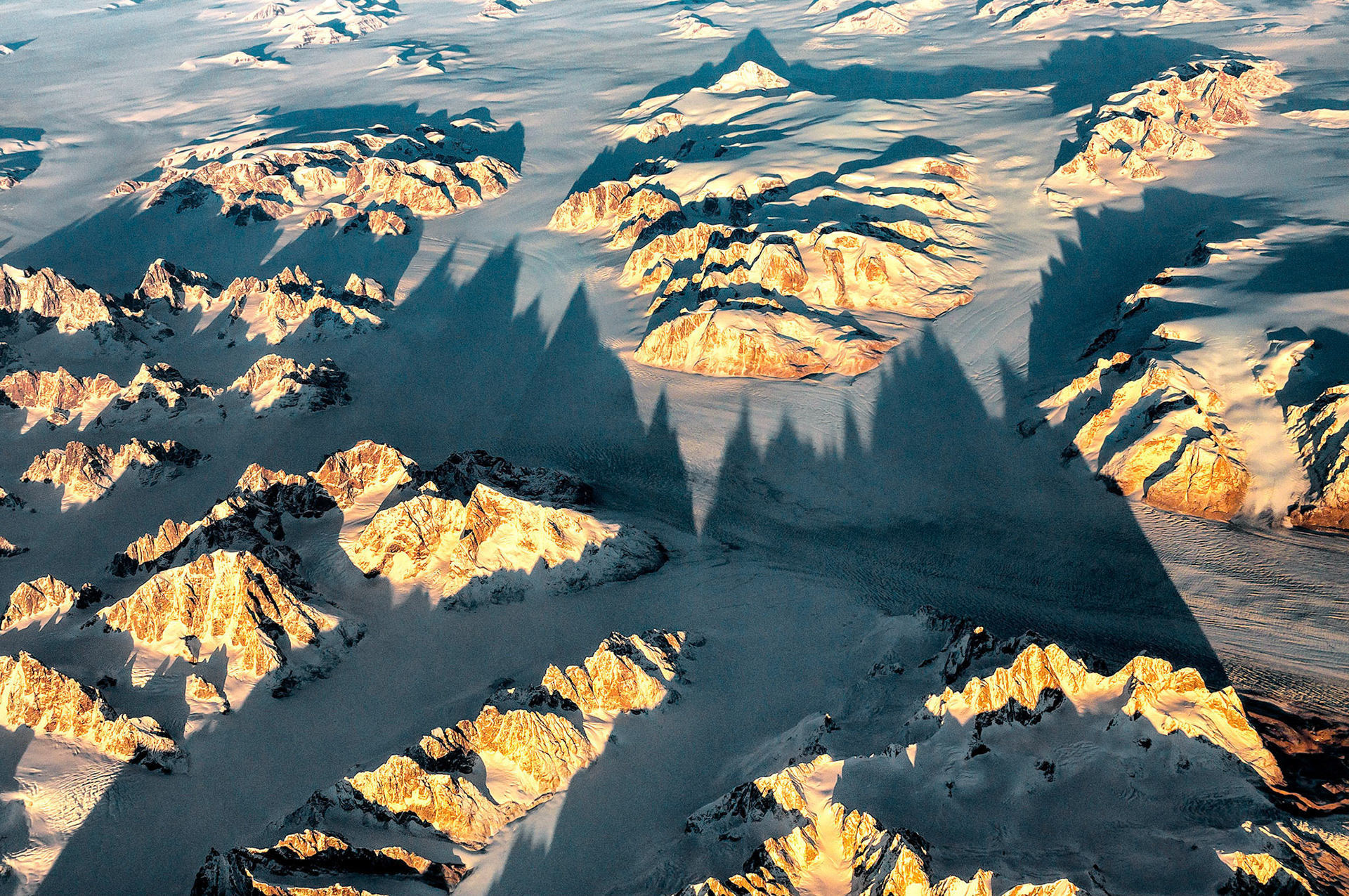 The dramatic ridges lines of these tall mountains cast their long shadows over rugged glacial terrain, somewhere over southern Greenland.