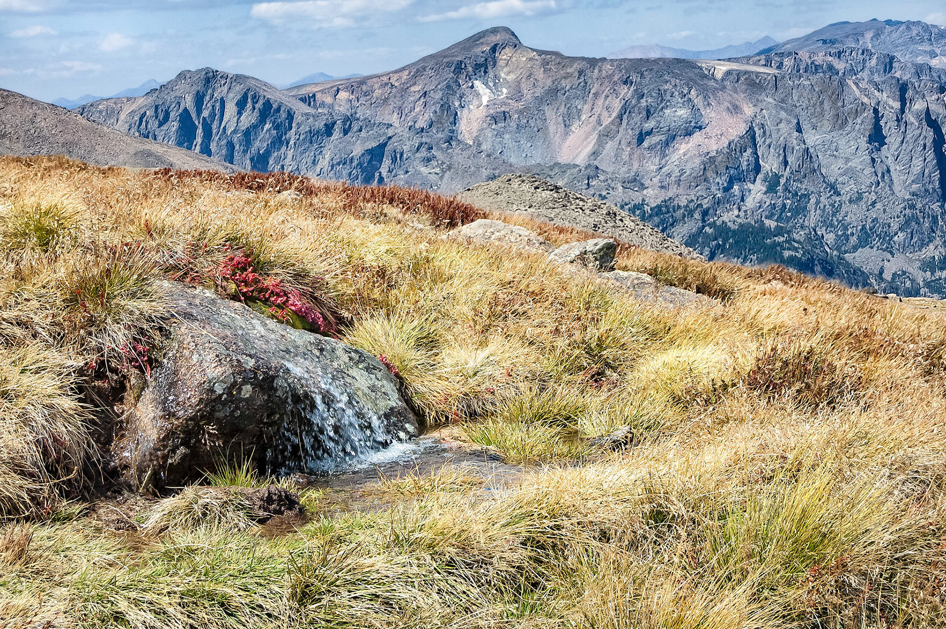 Runoff waters from recent rains in Colorado's Rocky Mountain National Park, cascade over a rocky ledge at Granite Pass. Grasses, burned by recent frosts, turn brown as shrubs begin to brighten with their autumn colors. Towards the west, the rugard skyline of the USA's continental divide rises above the valley floor.