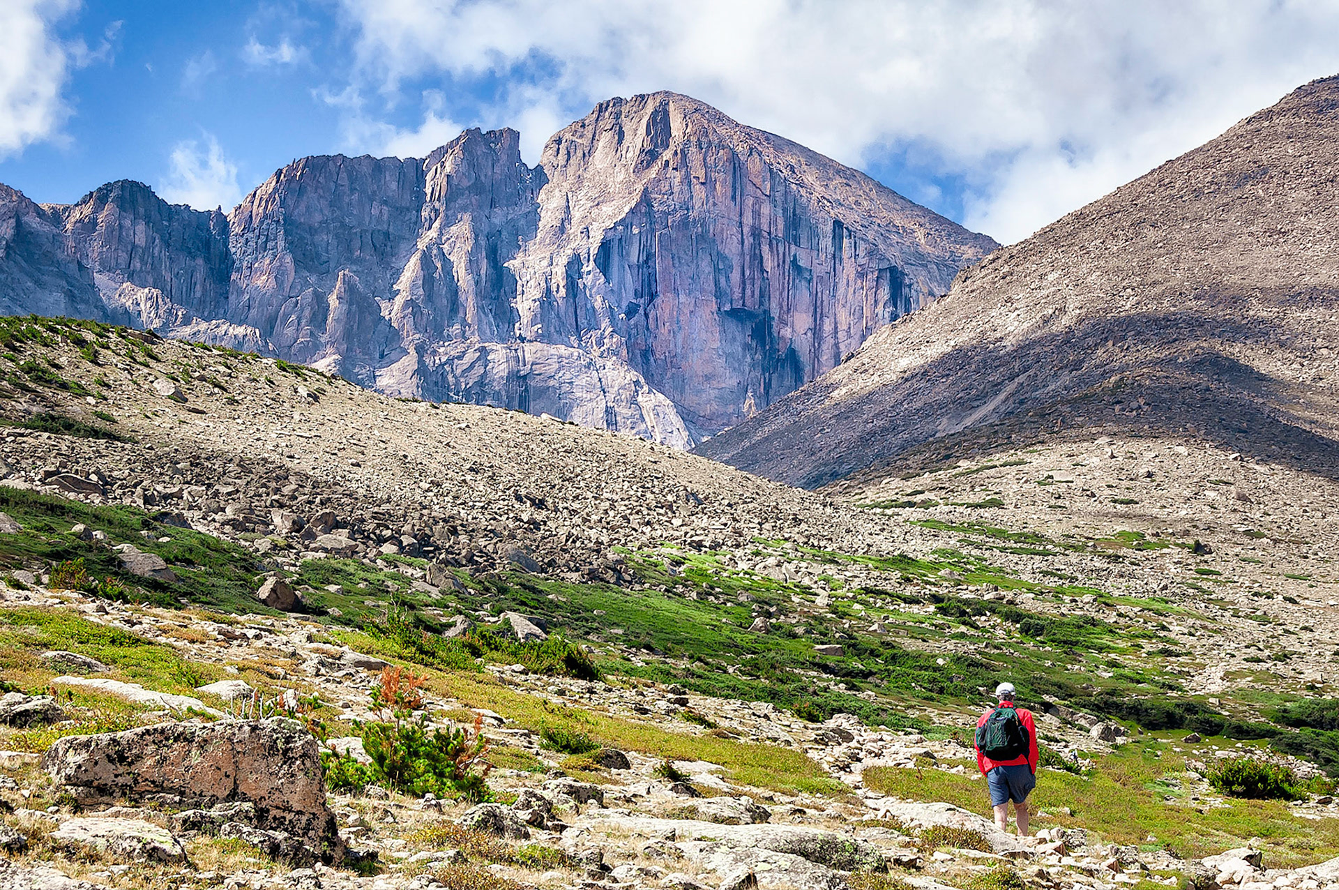 A hiker follows a rough  trail up to Granite Pass in the Rocky Mountain National Park, Colorado, USA. Longs Peak, (14,259 feet=4346 m) , one of Colorodo's famed "14ers", towers above in the distance behind the scree slopes of Mount Lady Washington, (13,281feet=4,048m).