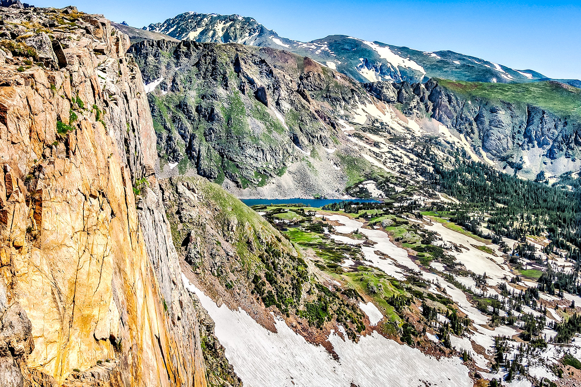 Breathtaking mountain scenery is common when hiking along the Rocky Mountain continental divide. This view is near Rollins Pass, Colorado, USA. In the valley below, winter snows are melting and in the distance, Devil's Thumb Lake glistens in the bright spring sunshine.
