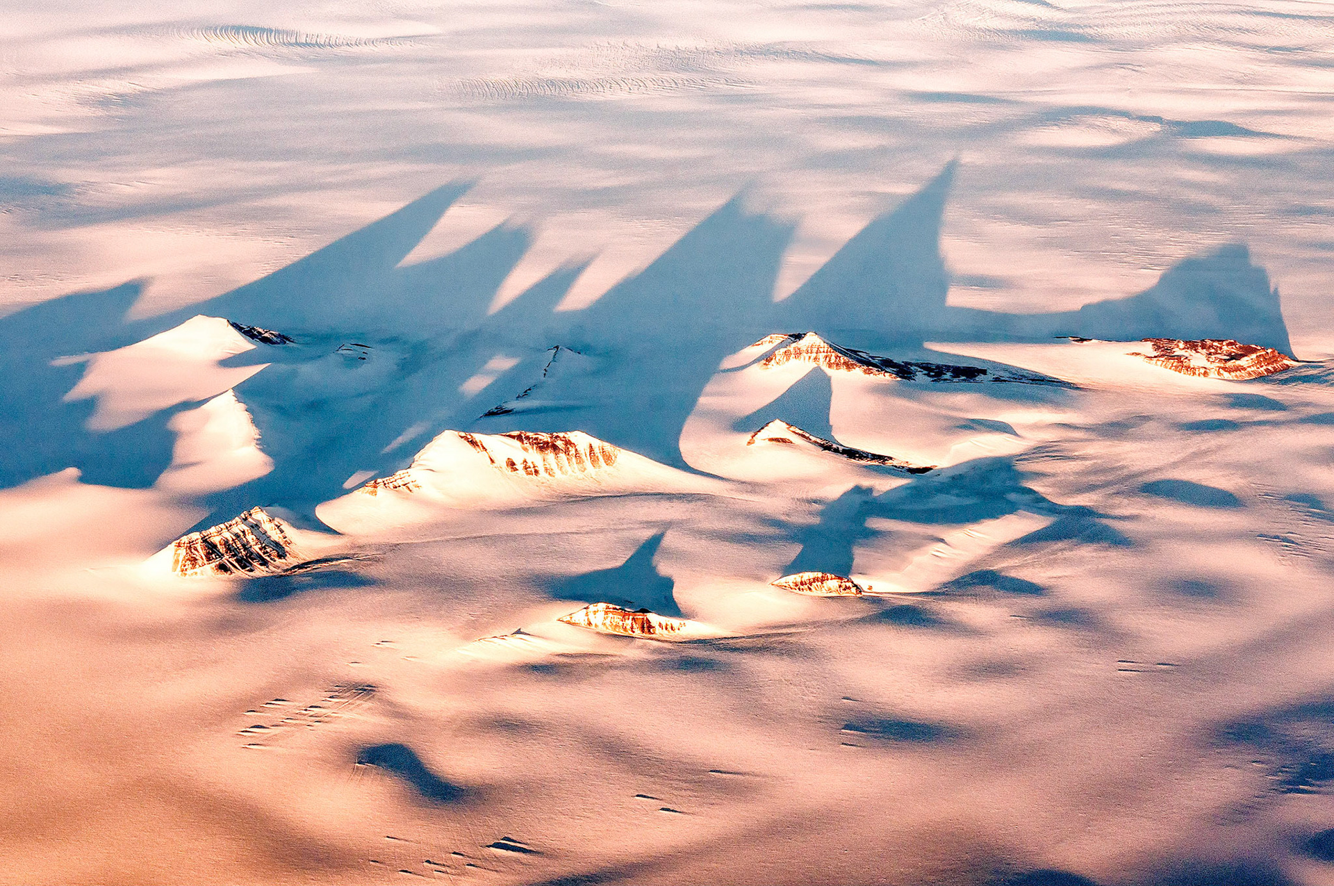 As the evening sun catches the tips of  high mountain peaks in eastern Greenland, long shadows are cast over the vast, frigid landscape.