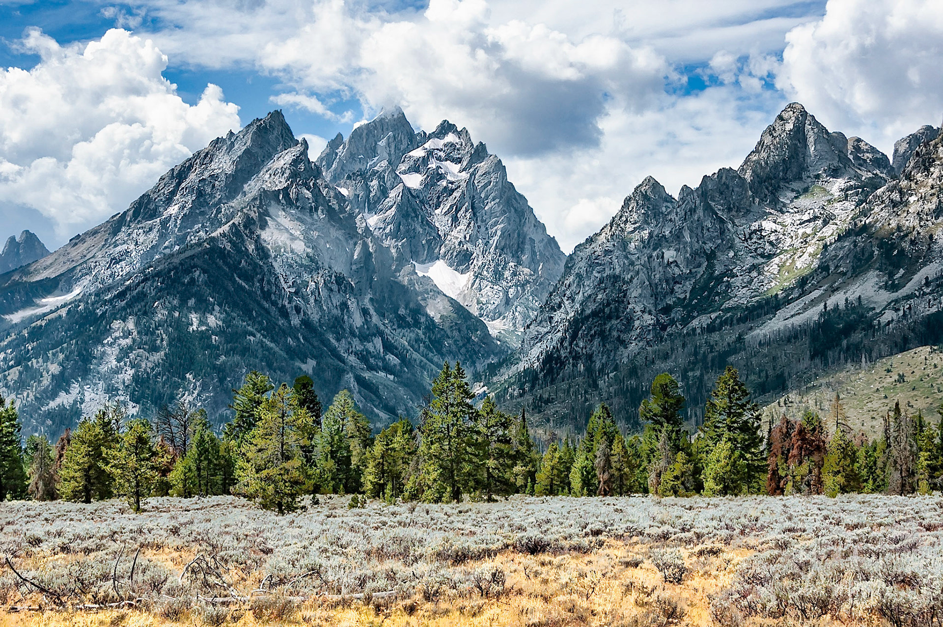 Passing clouds cast their shadows over peaks of the Grand Teton Ranges that arise abruptly and dramatically from sagebrush covered river flats near Jackson, Wyoming, USA. Grand Teton at 3,770 feet, (4,200 m), towers about 7,000 feet, (2130 m), above the valley floor.