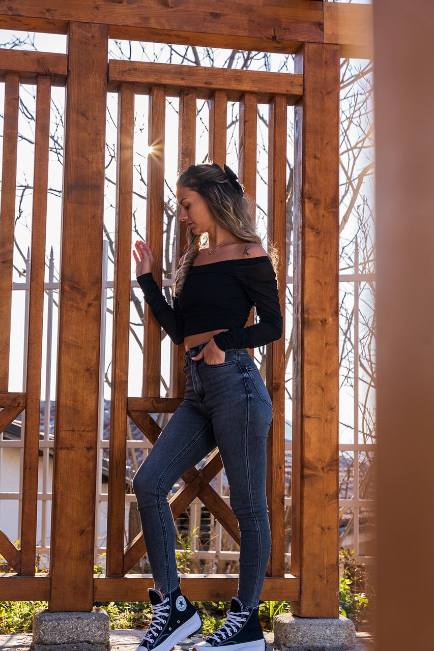 Profile fashion portrait at sunset, using a wooden lath structure to create leading lines toward the subject. Atmospheric visual storytelling by Arcane Media.