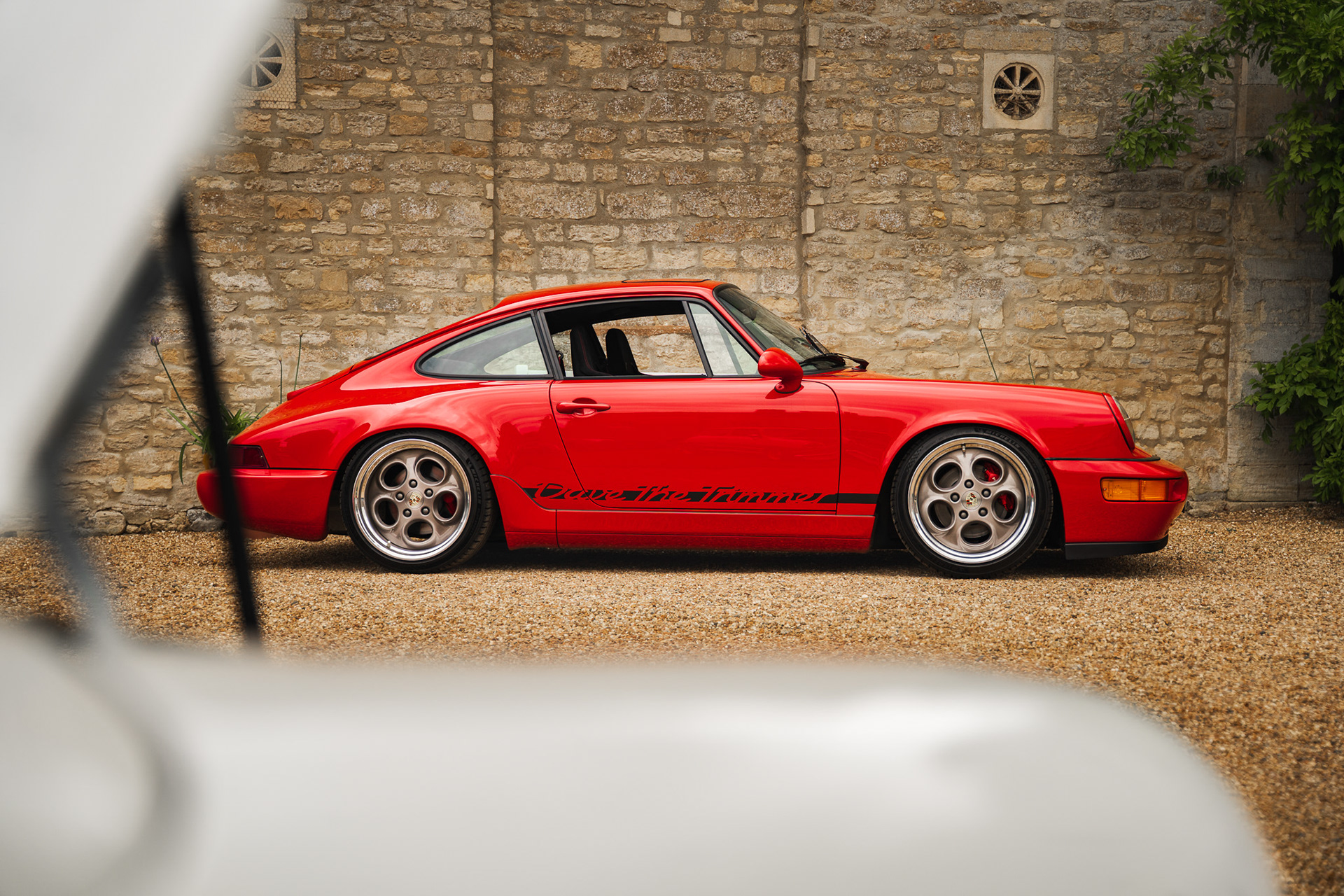 Classic red Porsche side profile parked against textured wall in UK