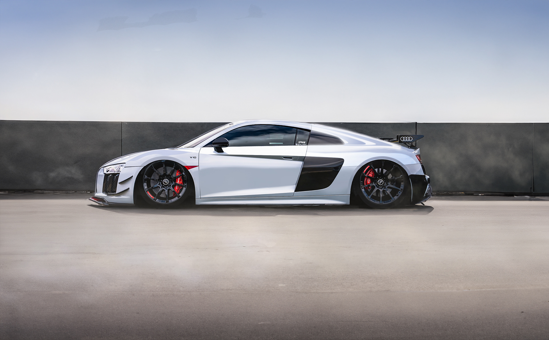 Expert composite and color correction for a modified, wide-body white Audi RS8 studio portrait. This advanced retouching emphasizes the race-inspired lines, contrasting red performance details, and clean matte/gloss textures. High-end custom car photography by Arcane Media