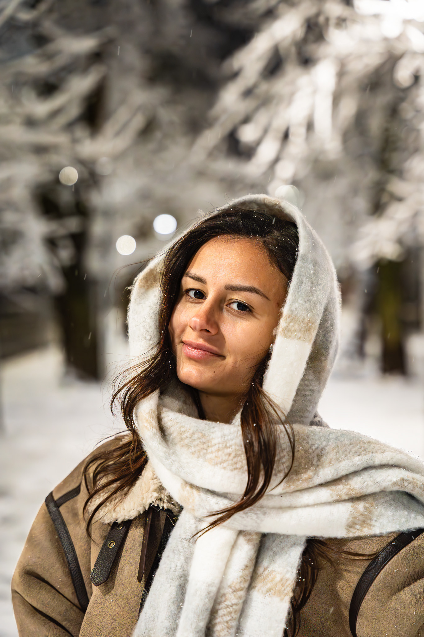 Close-up nighttime portrait of a brunette model wrapped in a large scarf with frost-covered branches in the background. Intimate lifestyle photography by Arcane Media, UK.