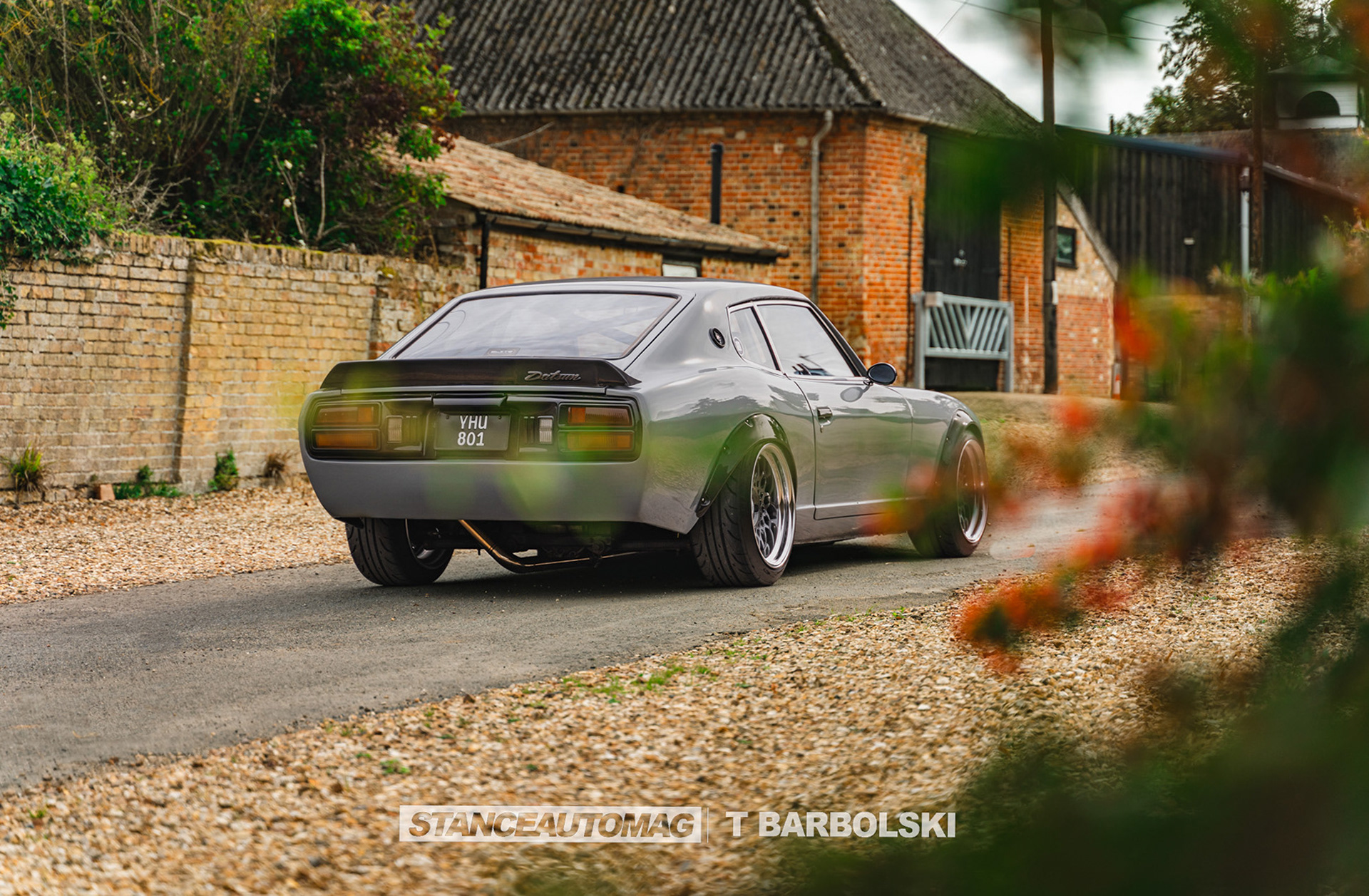 Modified Datsun 240z parked near stone wall with shallow depth of field