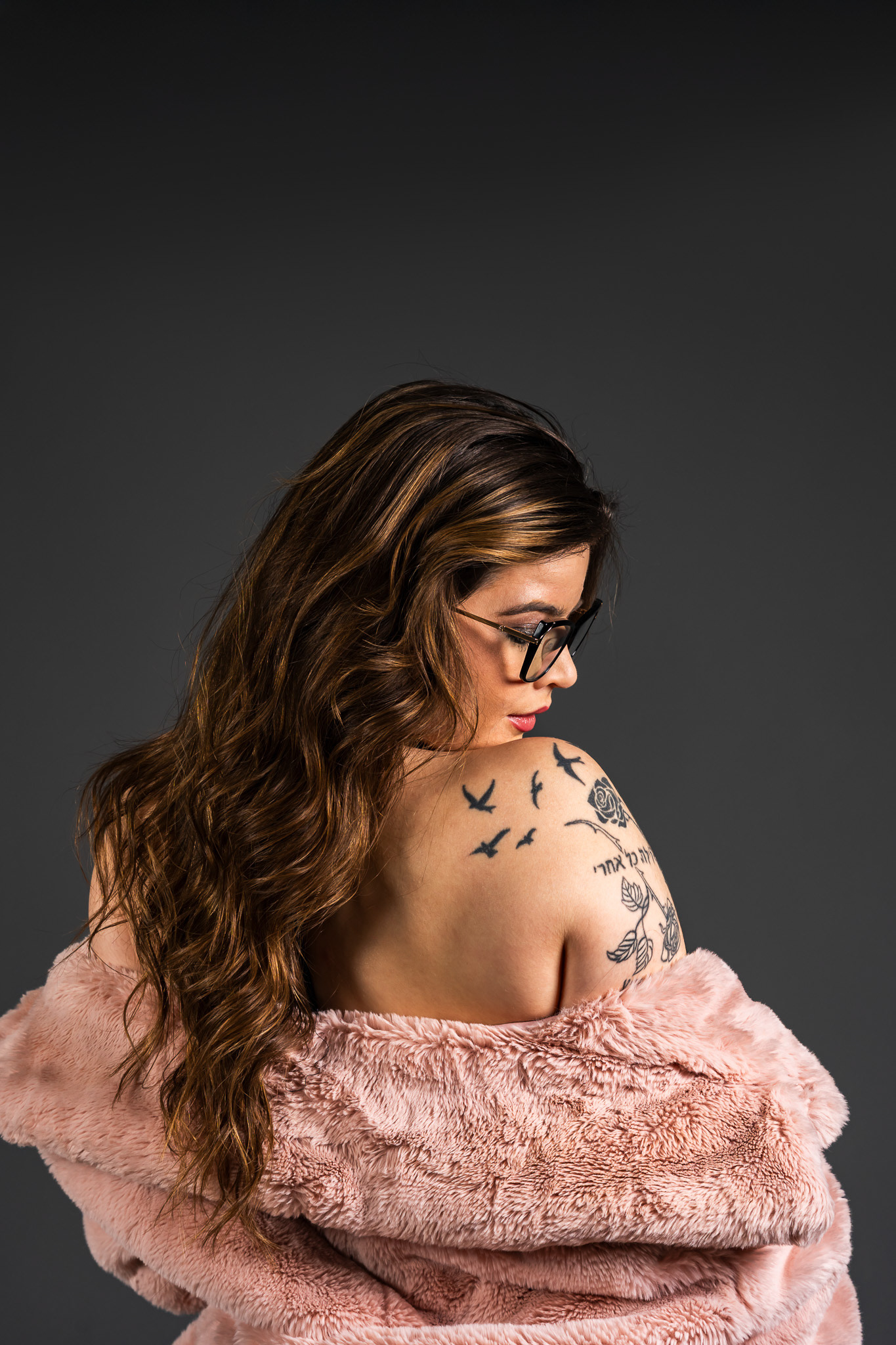 Alternative, closer composition of the high-end portrait featuring the model in the pink fur coat. Detailed macro shot focusing on the delicate tattoo work and the soft textures of the fur against deep, rich shadows. By Arcane Media