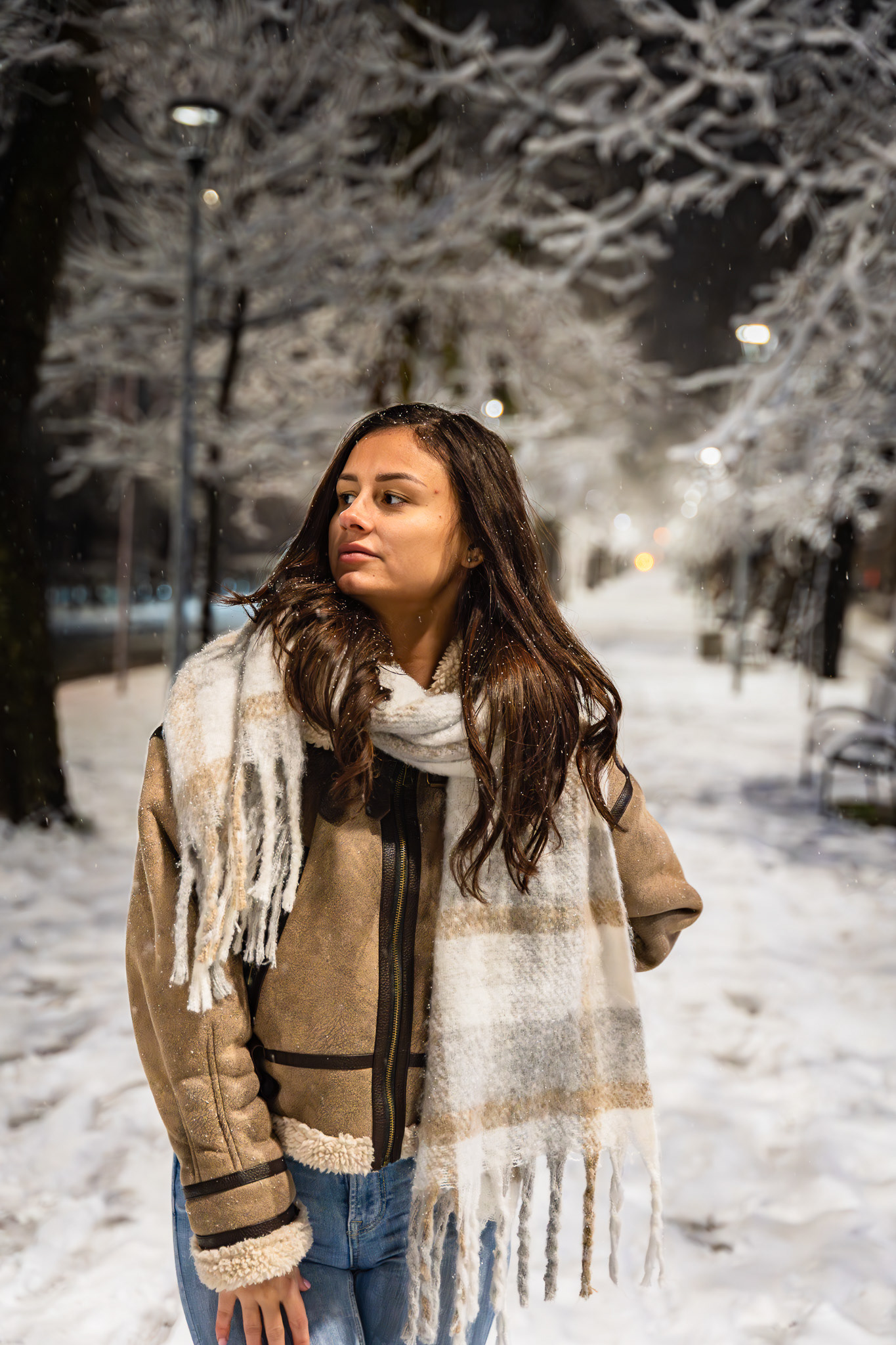 Close-up winter fashion portrait of a brunette model in a shearling jacket and scarf with bokeh street lights in the background. Photography by Arcane Media, UK.