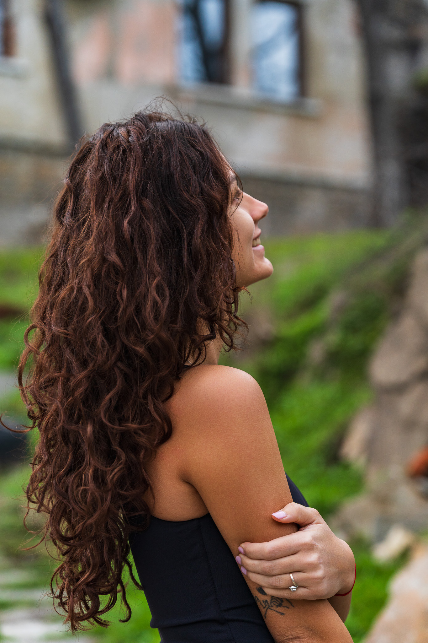 Candid portrait of a brunette model with voluminous curly hair in a black tank top against a lush green background. Lifestyle photography by Tenyo Barbolski.