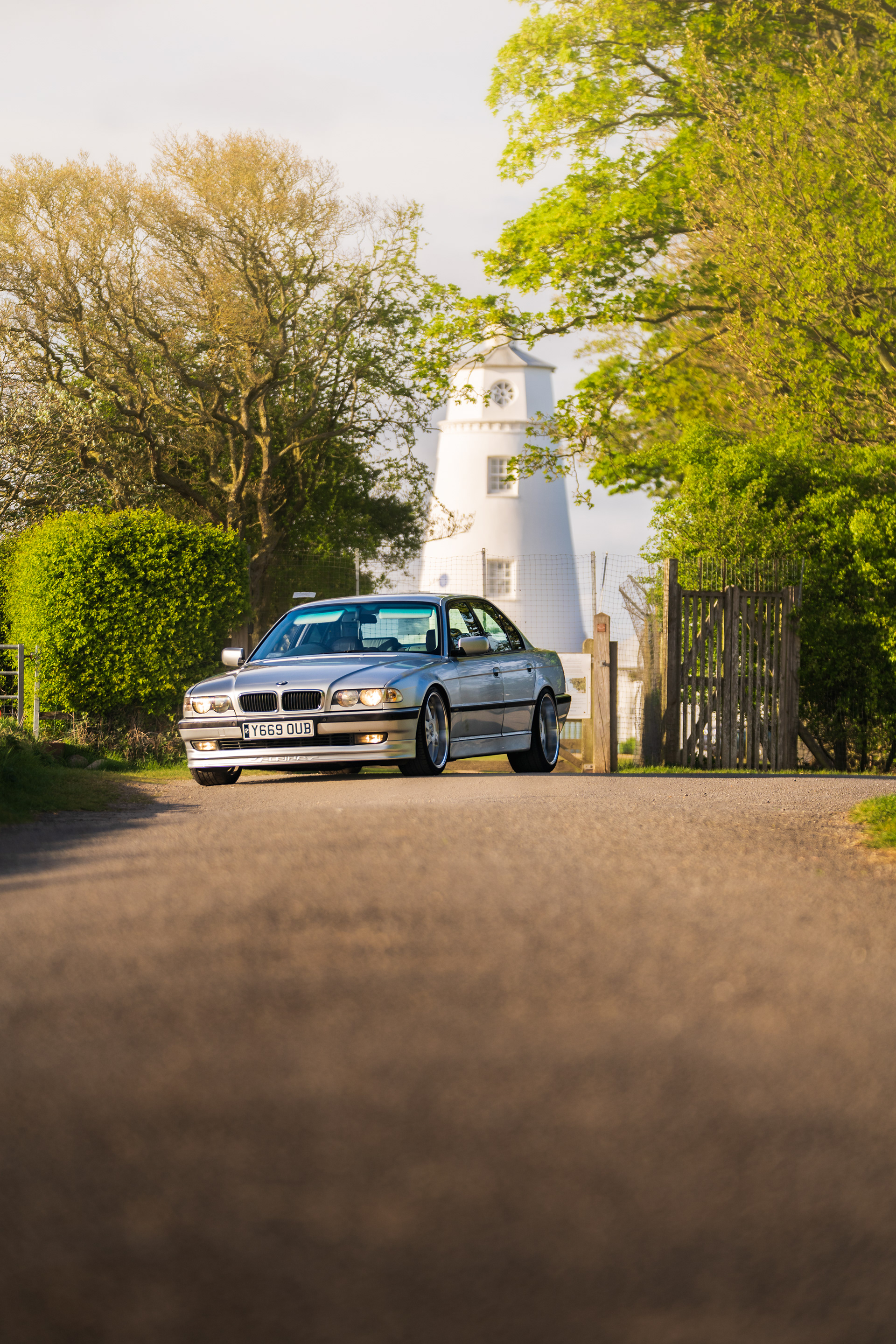 BMW 7 series e38 approaching through tree-lined road with soft natural lighting
