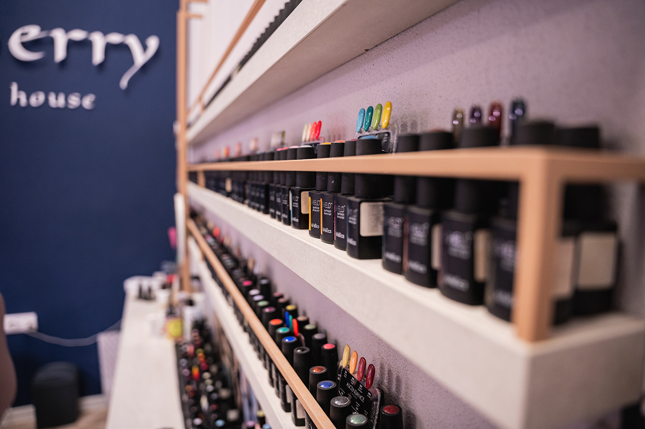 Impressive retail display photography featuring hundreds of professional nail polish bottles perfectly aligned on custom wall shelving. Visualizing the scale and variety of a premium beauty salon.