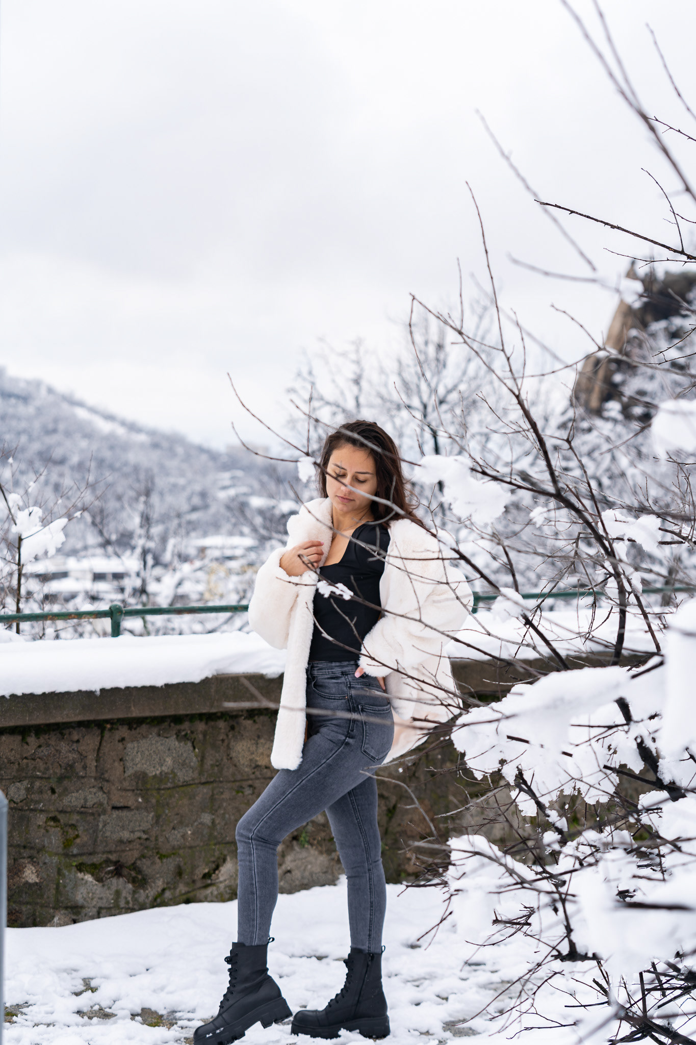 Full length winter lifestyle portrait of a female model in grey jeans and a white fur coat among snowy bare branches. Outdoor editorial photography by Arcane Media.