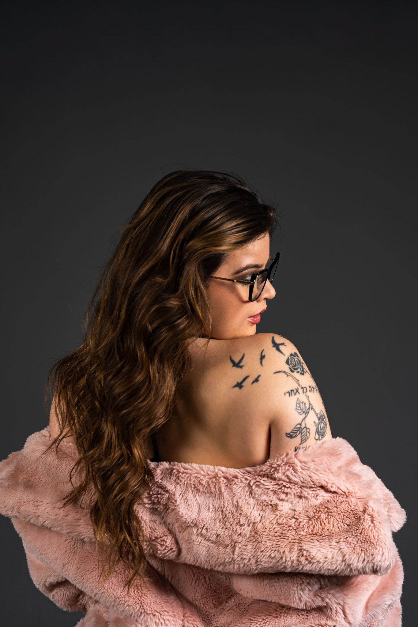 High-resolution, intimate portrait of a model looking away, framed by a luxury pink faux-fur coat and intricate shoulder tattoos. Expert low-light and shadow management create a sophisticated, 'Gothic Noir' or 'Cyberpunk' mood. Conceptual portraiture by Tenyo Barbolski.