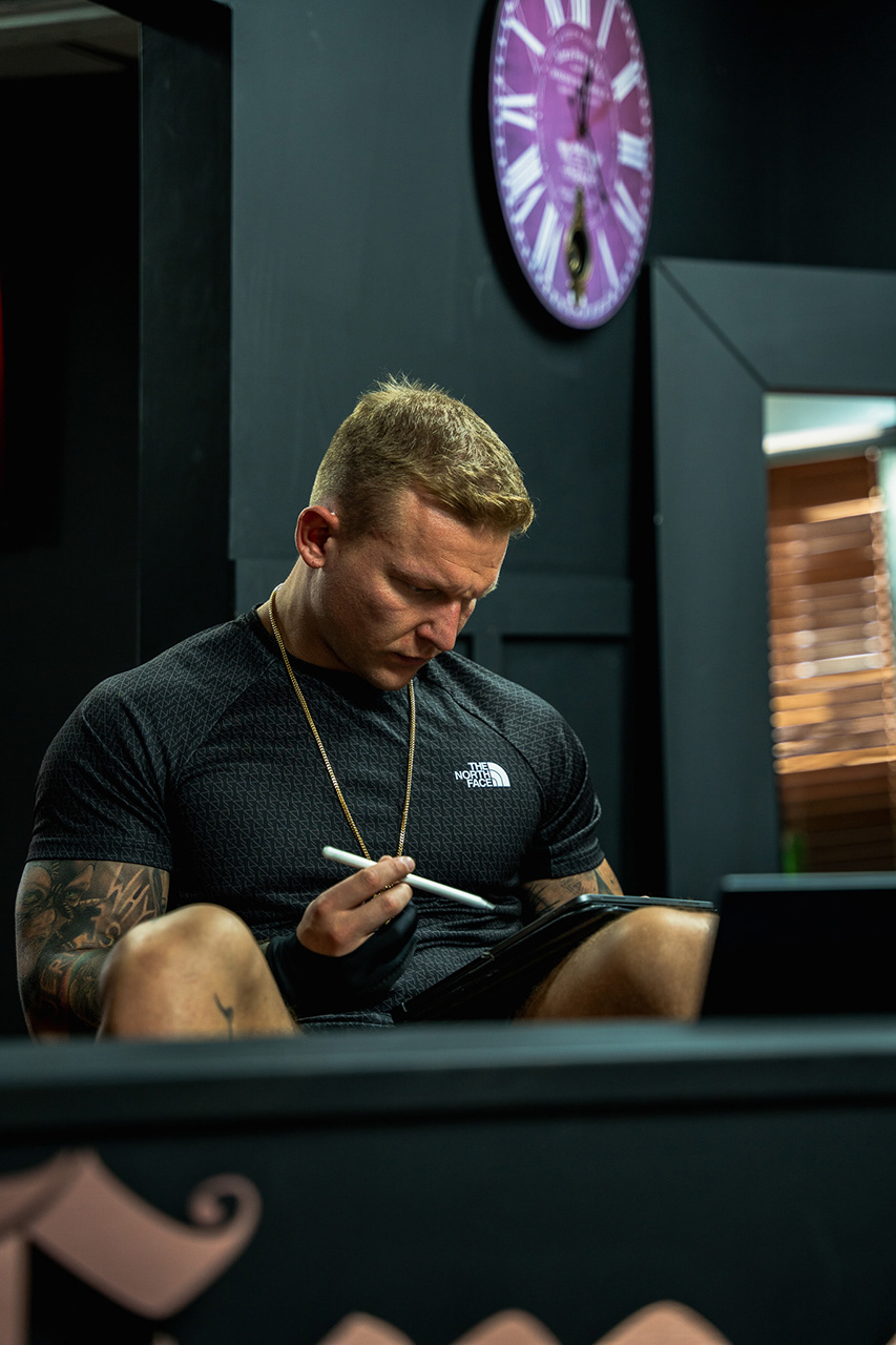 "Lifestyle branding photography of a male tattoo artist (leather jacket/tattoos) with his equipment in a low-key, professional studio setting. Focused on the creative process and character branding."