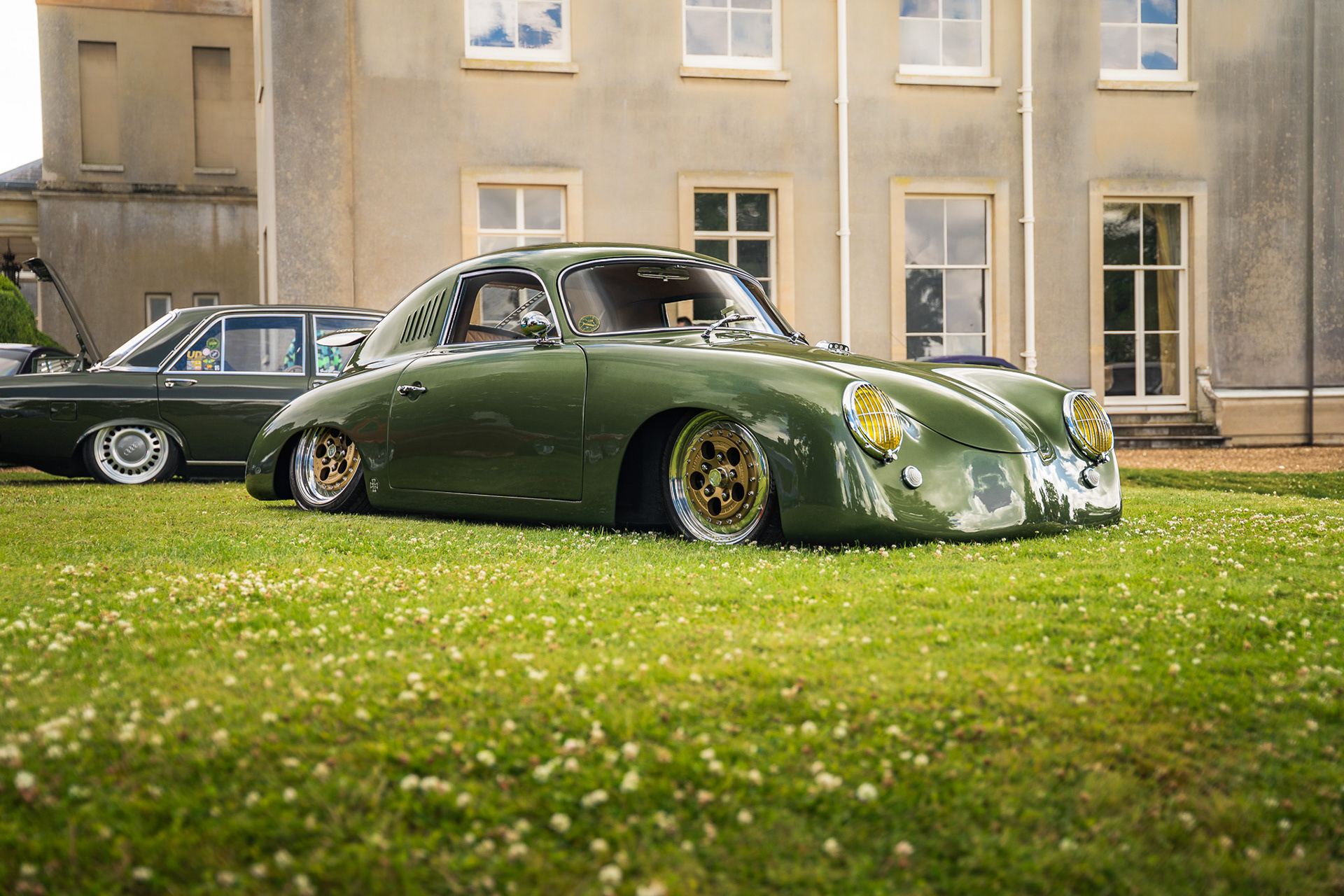 Low angle automotive photography of green modified car Porsche Outlaw 356 on grass with estate background