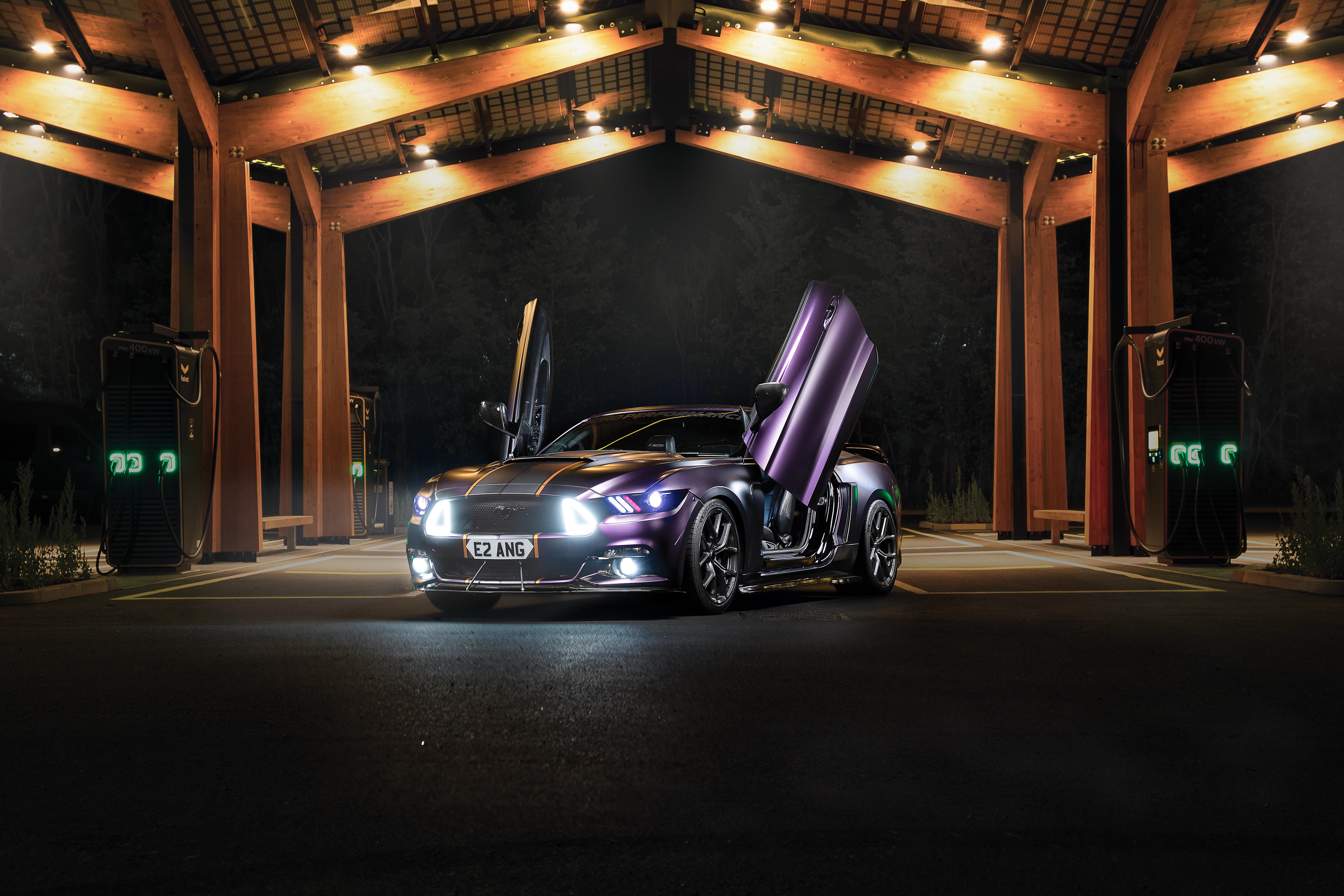 Futuristic automotive lighting composite and retouching of a Purple supercar Ford Mustang with Lambo-style doors open at an advanced EV charging station. This expert edit showcases seamless light blending of warm interior and cool futuristic lighting, highlighting innovation and advanced design
