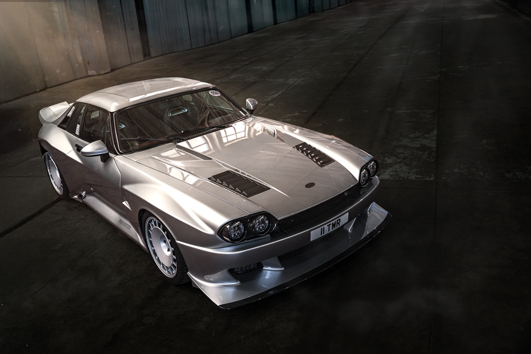 Specialist overhead automotive retouching of a silver modified classic sedan, TWR Supercat stance in a dramatic garage interior. This advanced edit features precise shadow control, clean perspective alignment, and high-fidelity texture enhancement of a unique custom car build. Displayed at Bicester Motion for Pistonheads Annual Meeting.