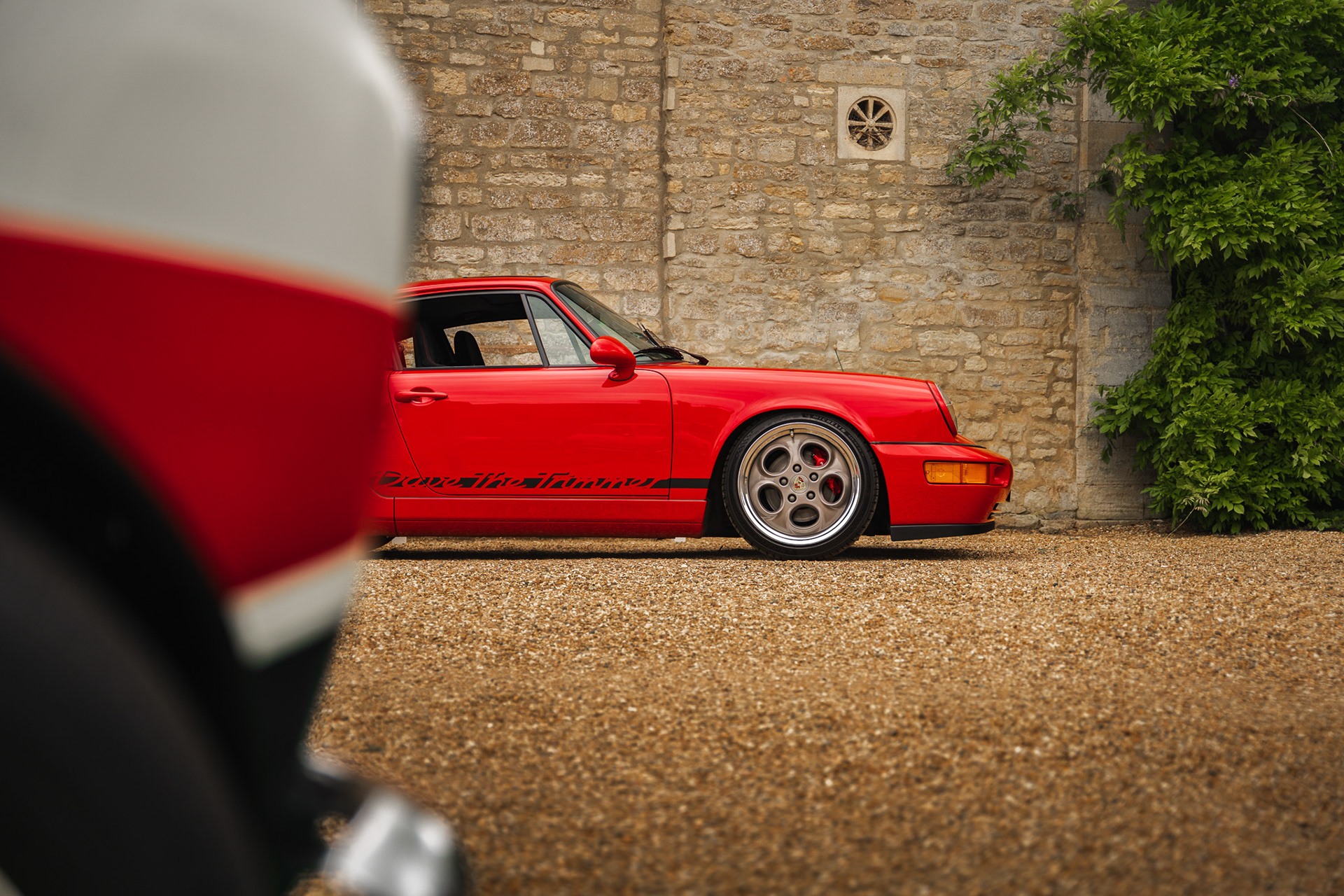 Framed automotive shot of red Porsche through foreground elements in urban setting