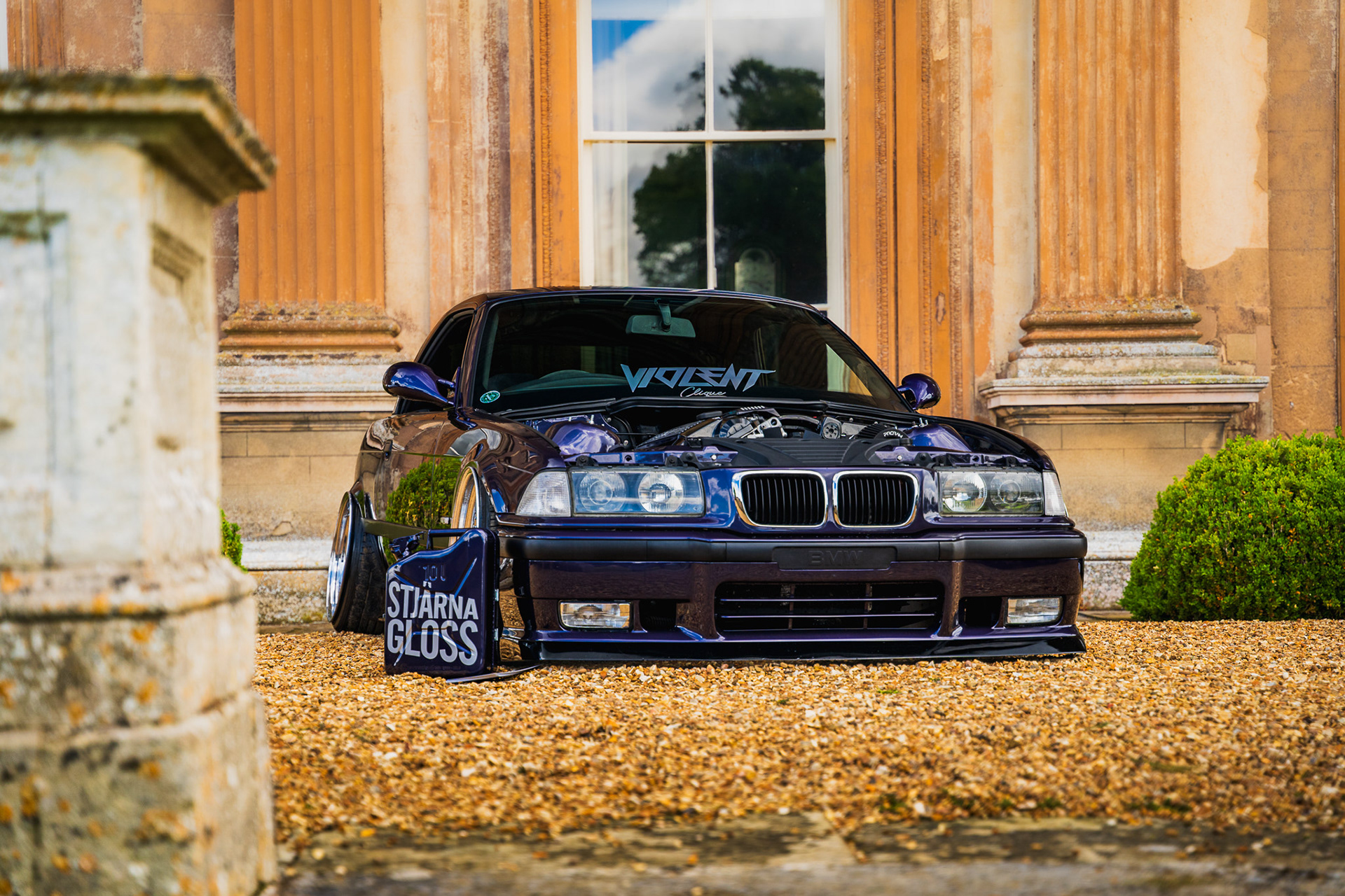 Front view of blue BMW e36 parked in front of architectural background