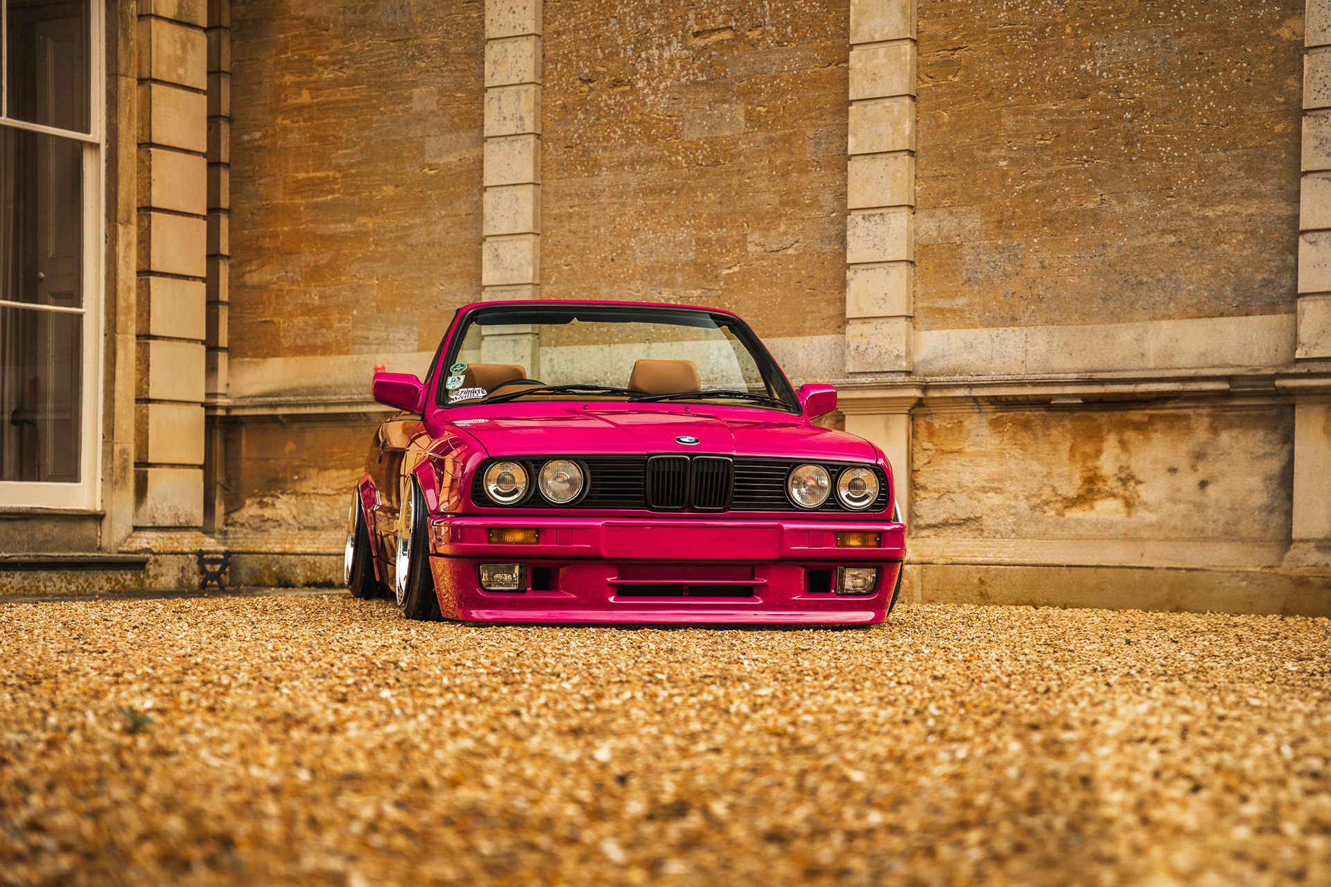 Front view of pink modified BMW e30 parked against textured wall