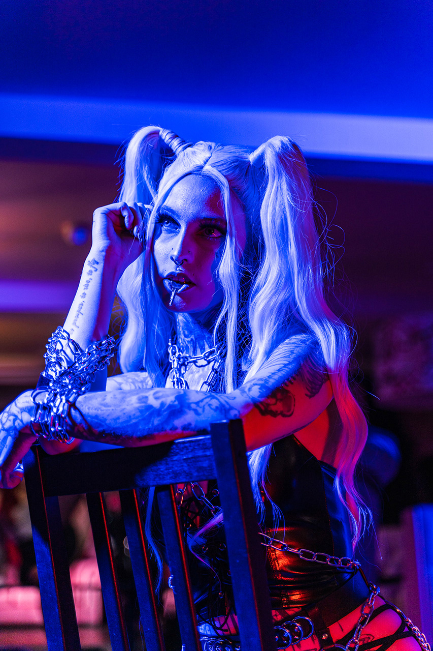 Cinematic conceptual portrait of a tattooed model utilizing saturated blue atmospheric lighting and low-key shadows to create a mysterious and rebellious mood. Expertise in technical color blending by Arcane Media.