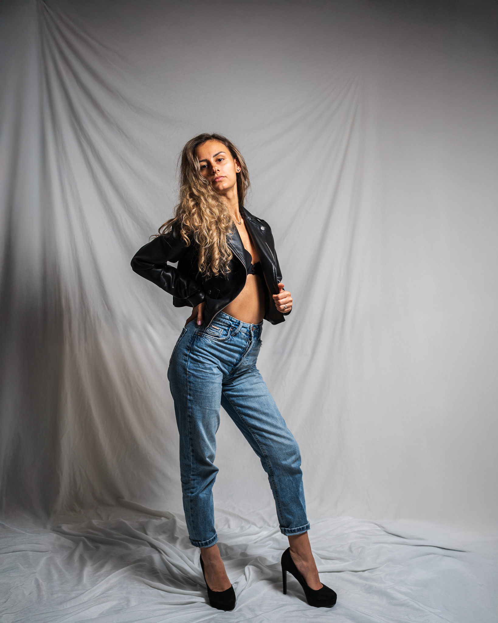 Confident studio fashion portrait of a model in a black leather jacket and jeans. The use of leading lines in the draped fabric background creates a professional, commercial aesthetic suitable for apparel branding. Shot by Arcane Media