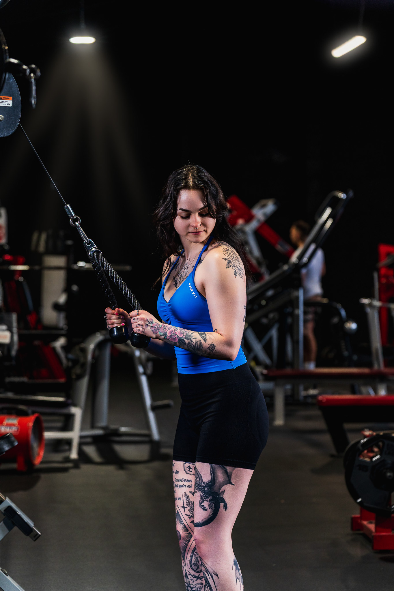 Editorial fitness photography of a tattooed female model in a professional gym setting. Cinematic lighting and composition by Arcane Media, Cambridgeshire.