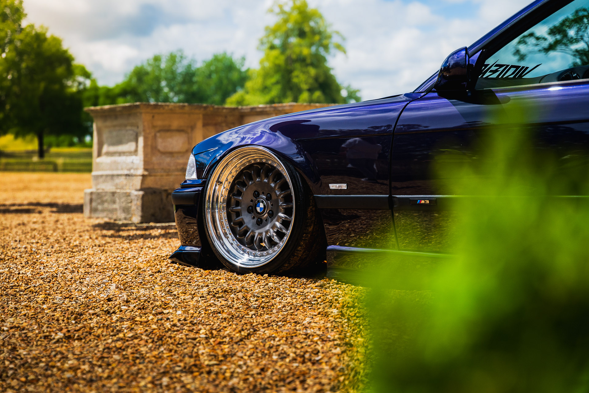 Blue sports car BMW e36 partially hidden behind foliage with shallow depth of field