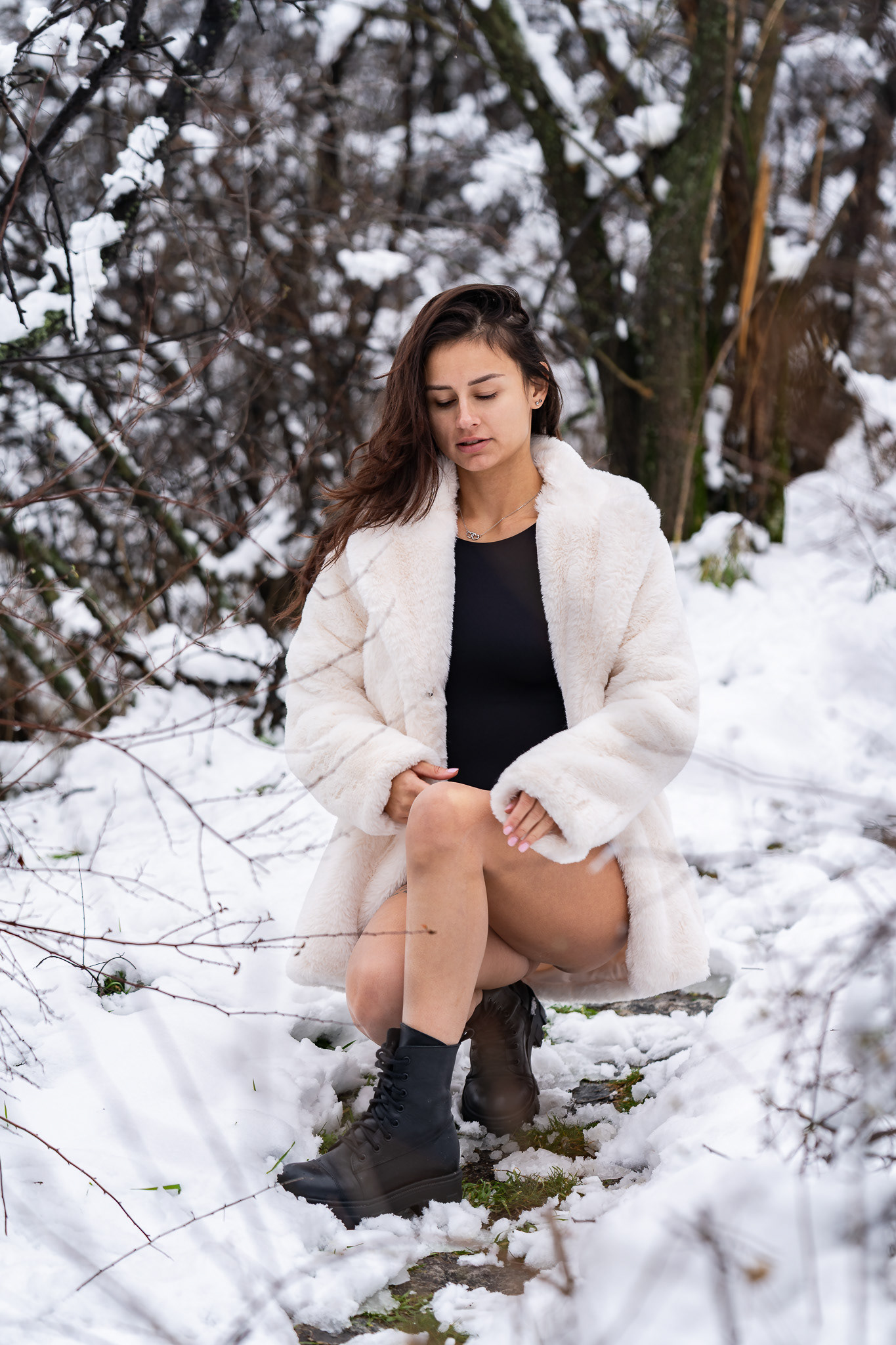 Editorial winter portrait of a brunette model in a white fur coat standing among snow-laden branches. Cinematic natural light photography by Tenyo Barbolski.