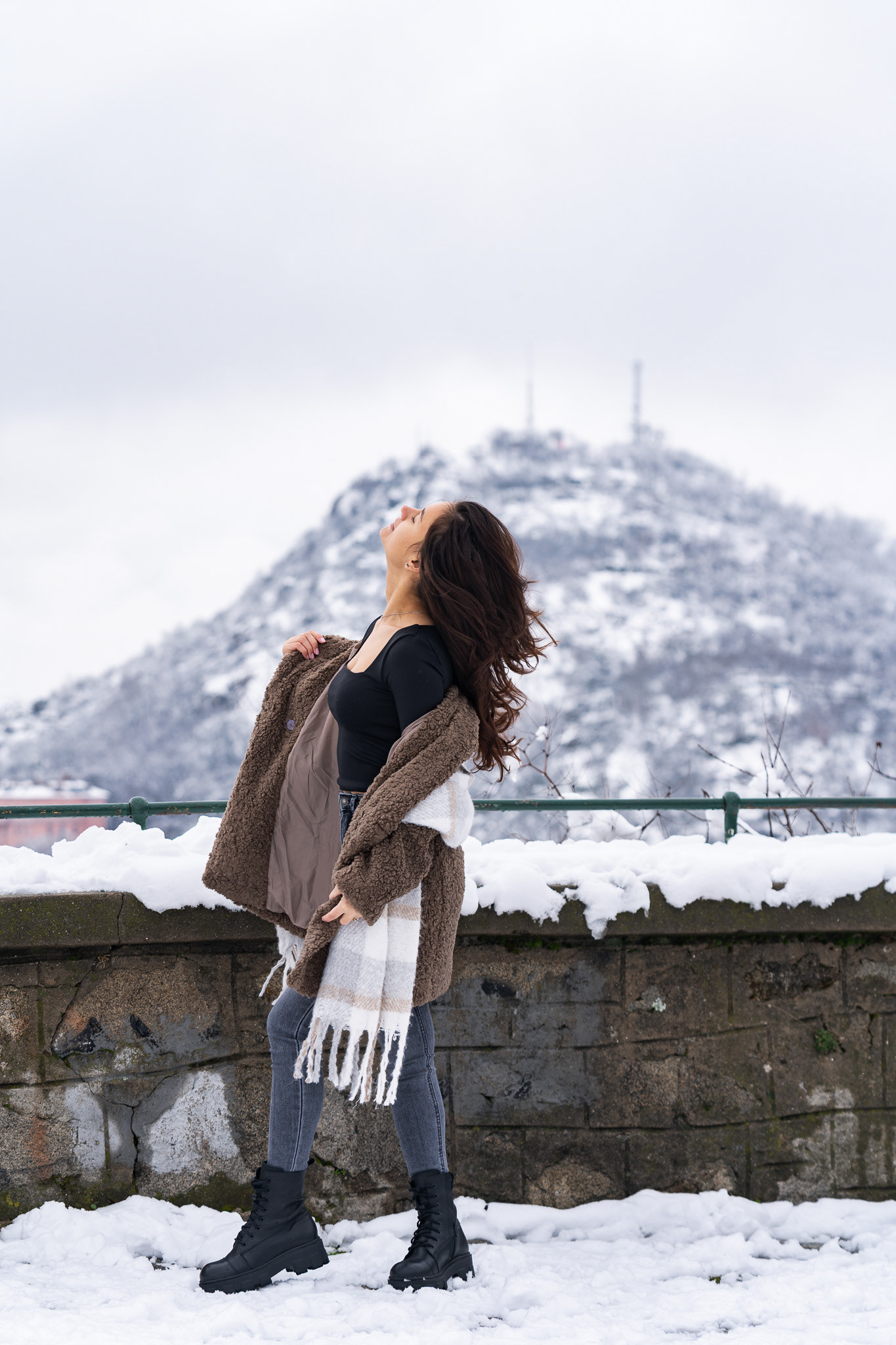 Dynamic winter editorial of a female model in a shearling coat with hair blowing in the wind against a snowy mountain landscape. Photography by Tenyo Barbolski.