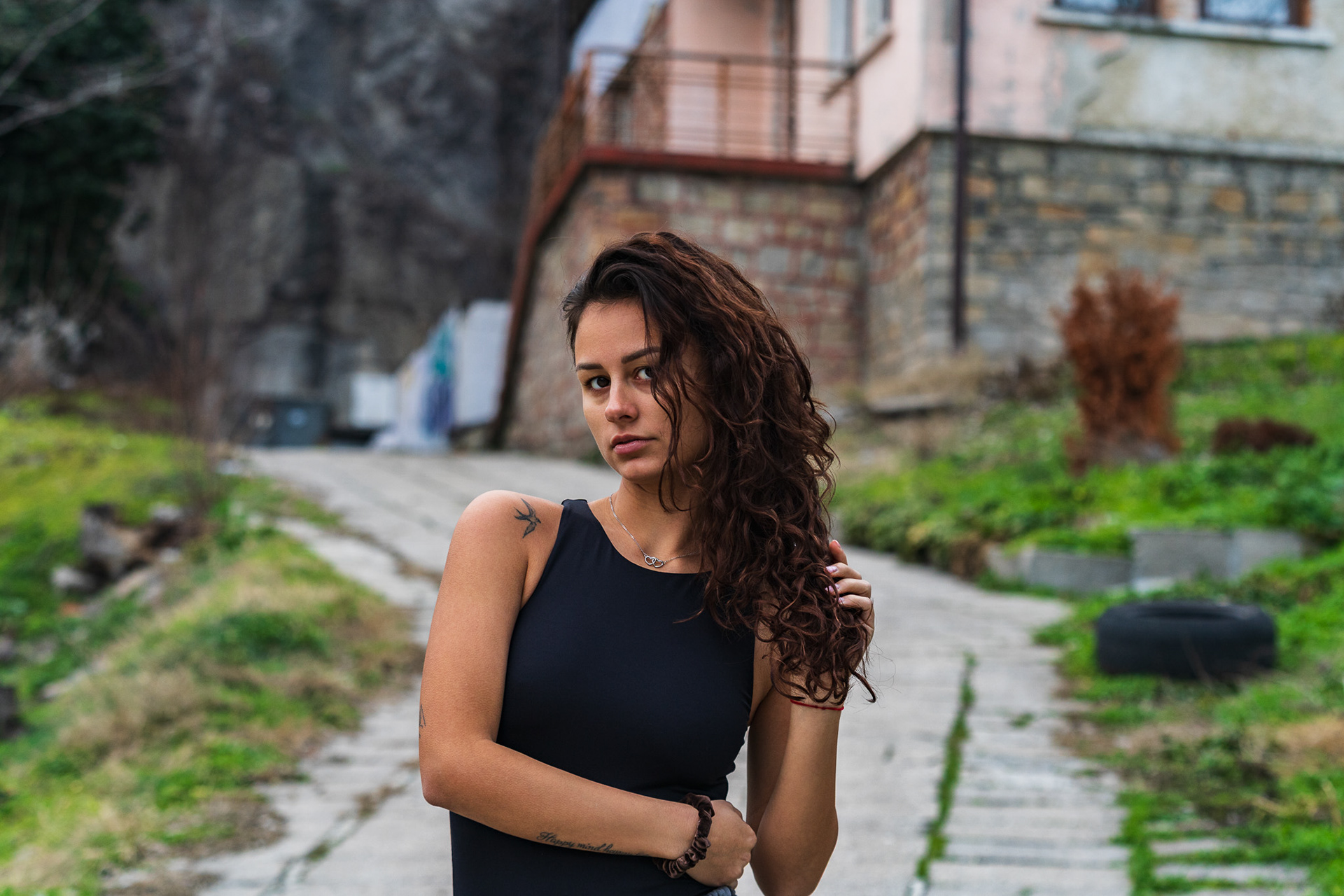 Natural light fashion portrait of a female model in a black top against a green hillside and traditional architecture. Editorial photography by Arcane Media.