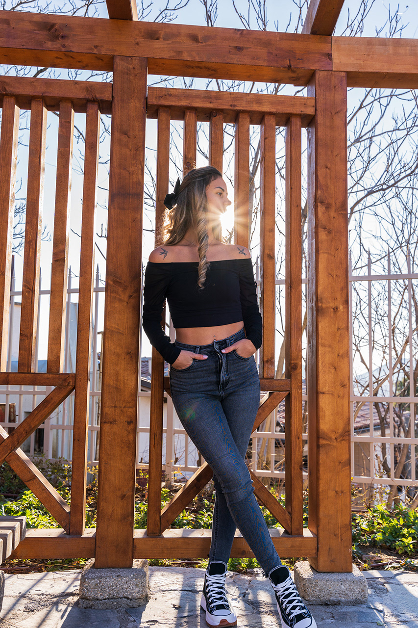 Symmetric fashion shot under a wooden structure with the sun peeking through. A masterclass in natural light control and geometric composition.