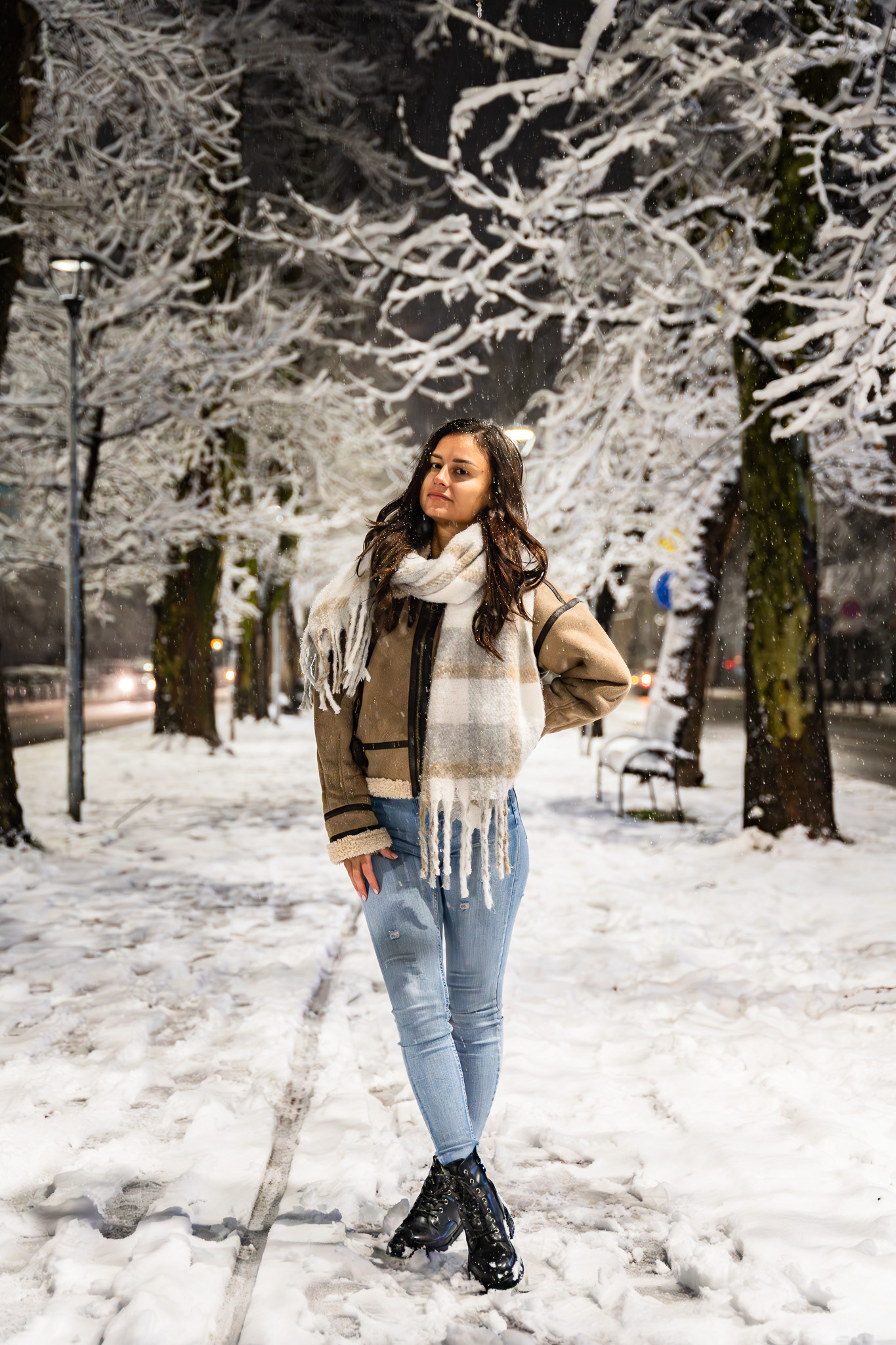 Full length winter fashion portrait of a female model in a tan coat and scarf walking on a snow-covered path with a mountain backdrop. Photography by Tenyo Barbolski.