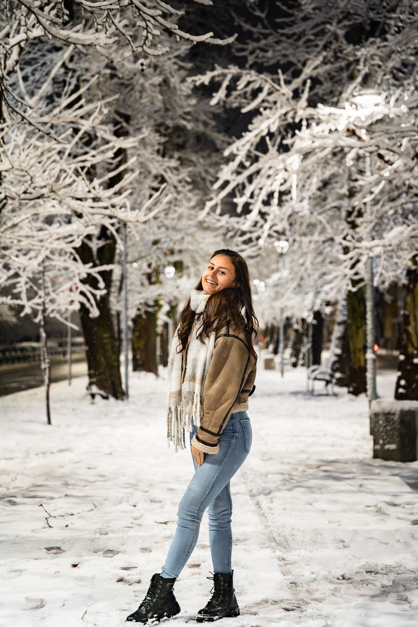 Atmospheric nighttime portrait of a female model in winter fashion looking upward among snow-laden trees. Cinematic lifestyle photography by Tenyo Barbolski, UK.
