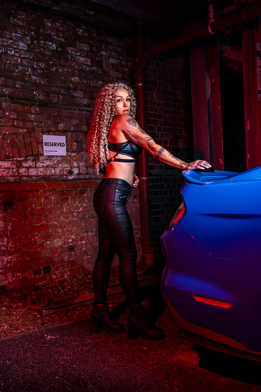 Commercial automotive and fitness lifestyle photography featuring a gym model in streetwear attire. This shot emphasizes the athletic silhouette and 'power' aesthetic of both the model and the Mustang. Specialist lighting by Arcane Media.