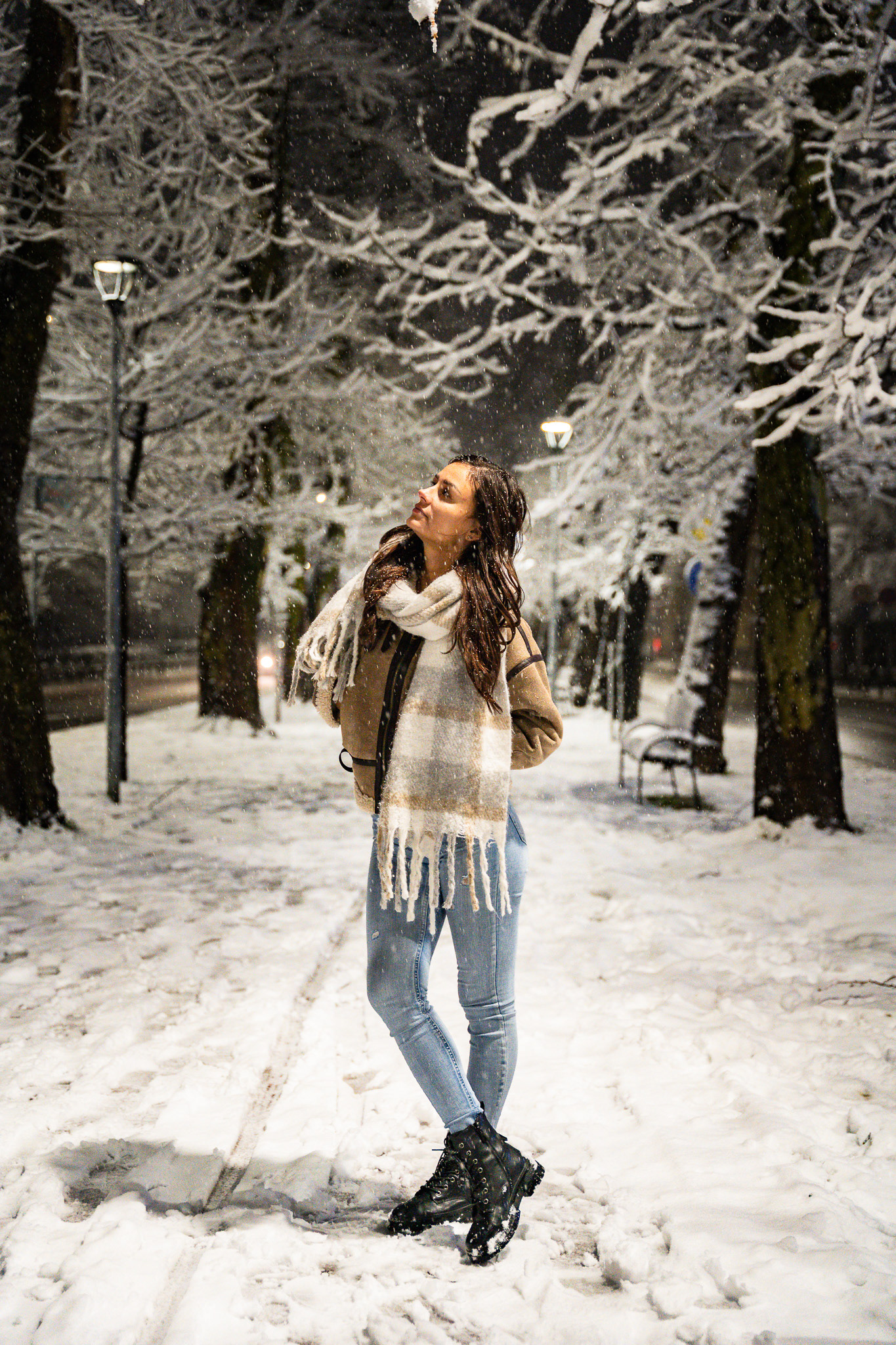 Winter lifestyle fashion portrait of a brunette model in a shearling coat and scarf on a snowy promenade with frost-covered trees. Editorial photography by Arcane Media, UK.
