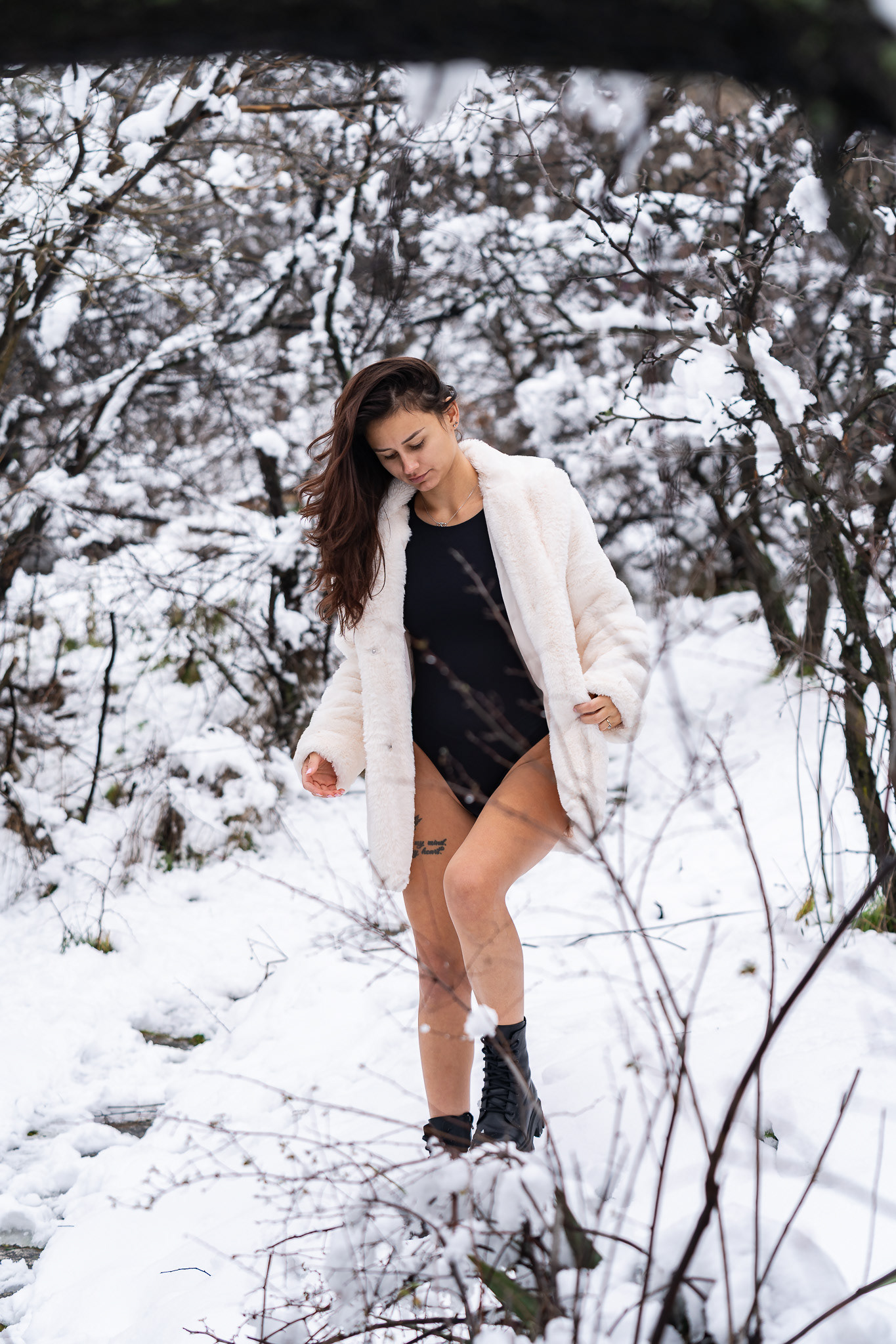 Fashion portrait of a curly haired female model in a white fur coat posing dynamically in a snowy woodland setting. Editorial photography by Arcane Media.