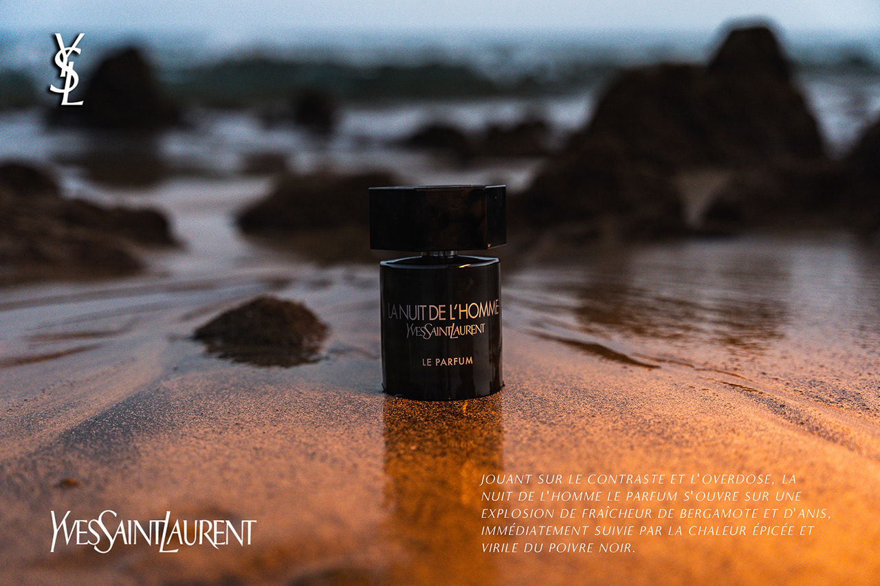 Detailed Golden Hour commercial product photography of an open Yves Saint Laurent (YSL) perfume bottle resting on wet beach sand. Capturing texture contrast, color grading, and accurate product reflections.