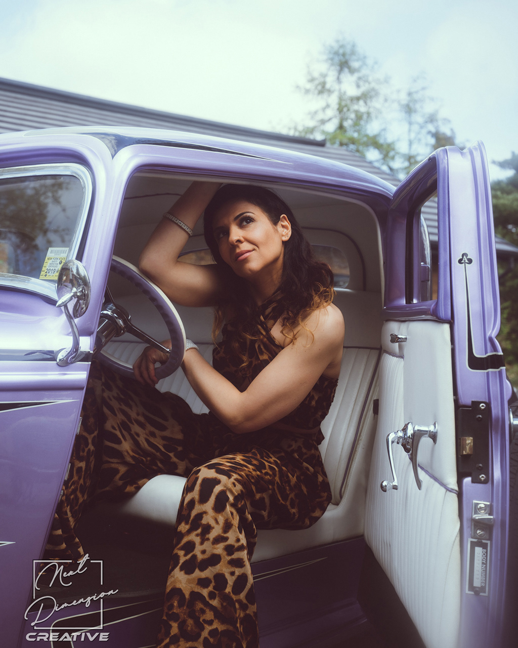 Interior portrait of a model seated in a vintage vehicle. Soft-focus lighting highlights the luxury textures of the classic car upholstery and the model's expression.
