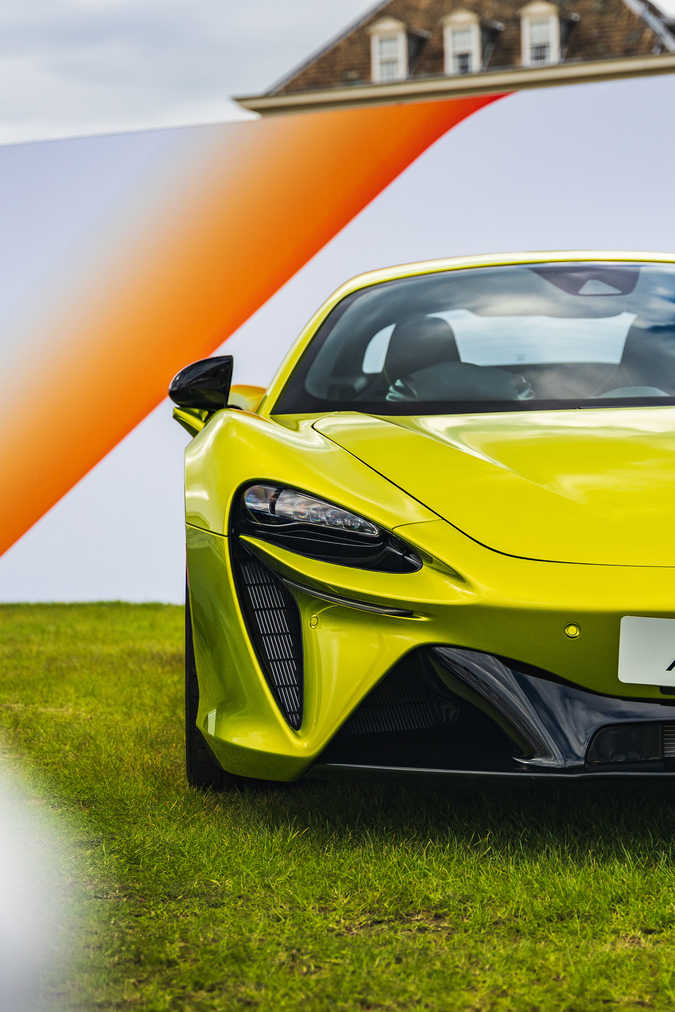 Green car McLAren Artura close up in modern garage with grass 